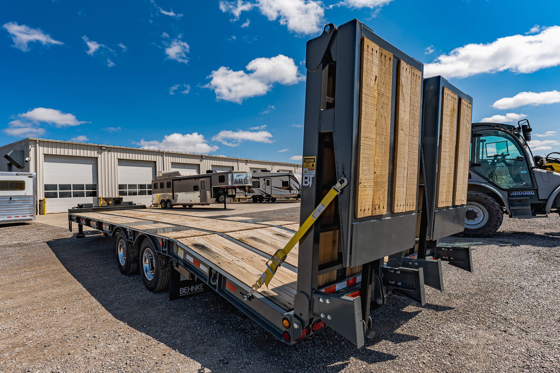Flatbed trailer loaded with timber boards in an outdoor industrial yard under a bright blue sky