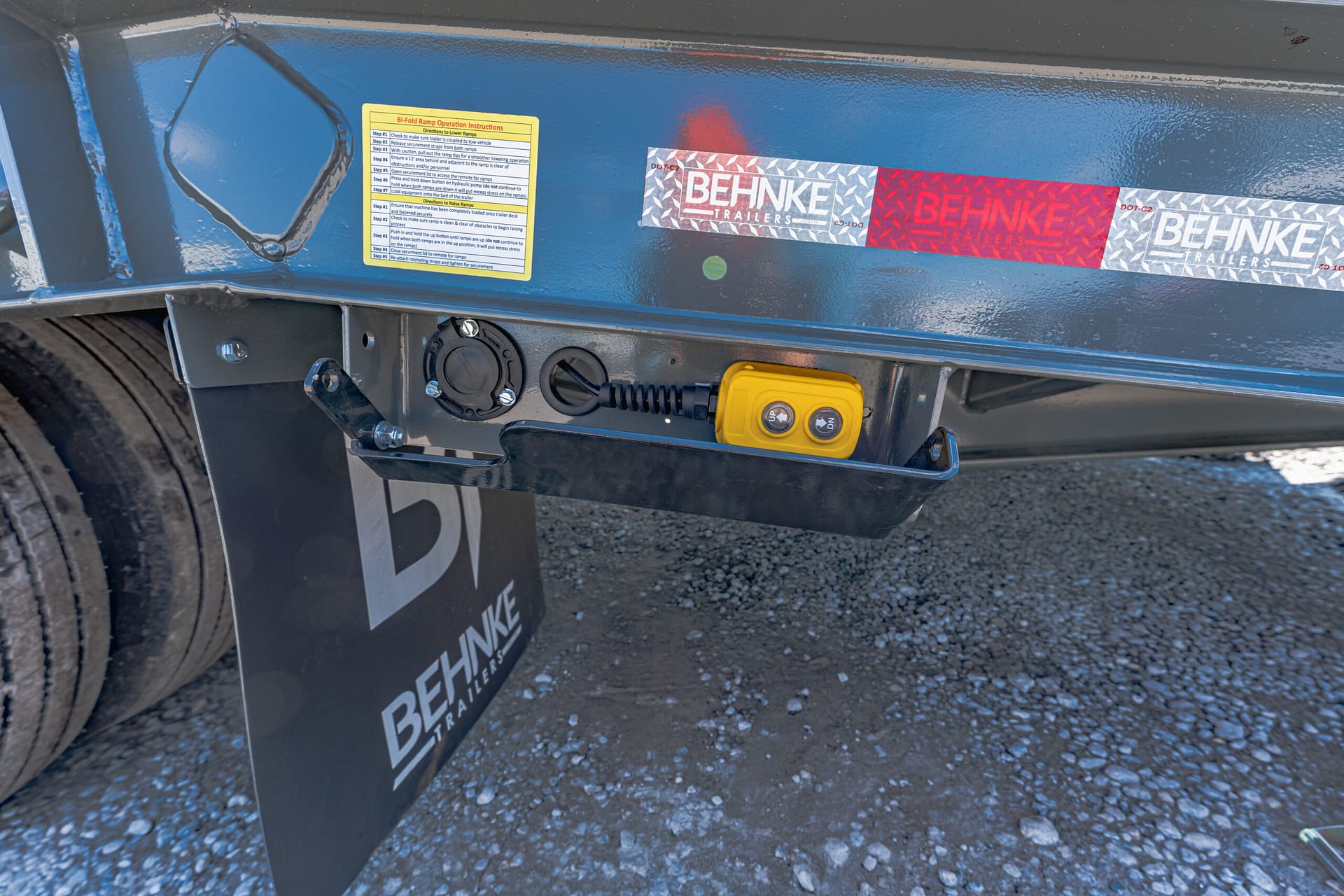 Close-up of a blue trailer with a yellow control pendant, circular port, and Behnke Trailers branding sticker on the side panel.