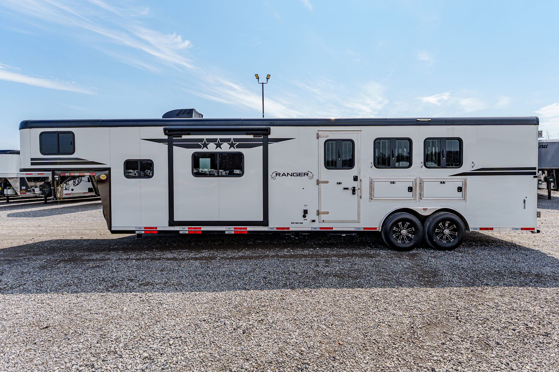 White Ranger horse trailer with black star graphic, side windows, and two-axle wheels on gravel lot.