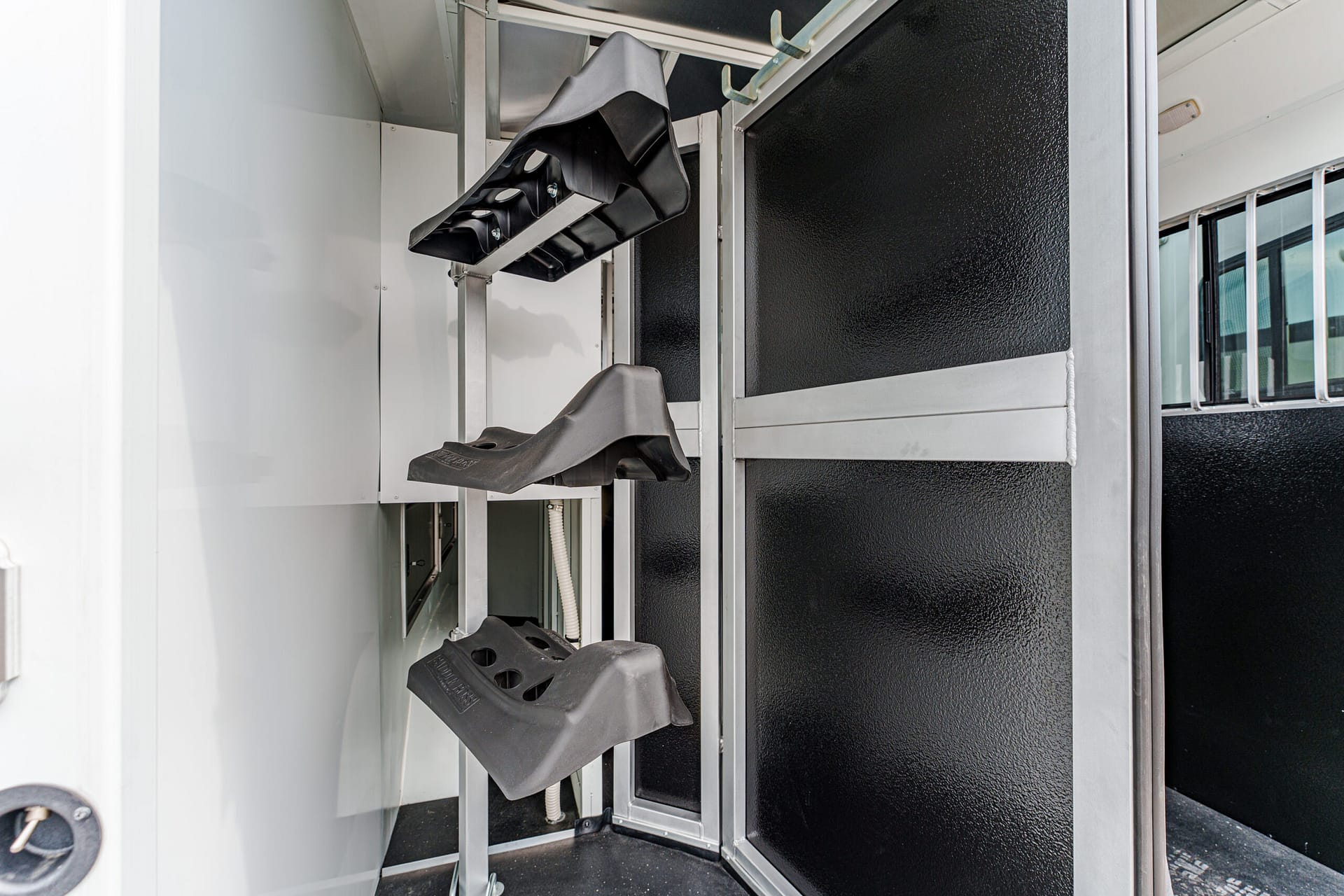 Narrow interior view of a metal rack with three black plastic holder cups mounted on a vertical rail inside a trailer or cabinet.