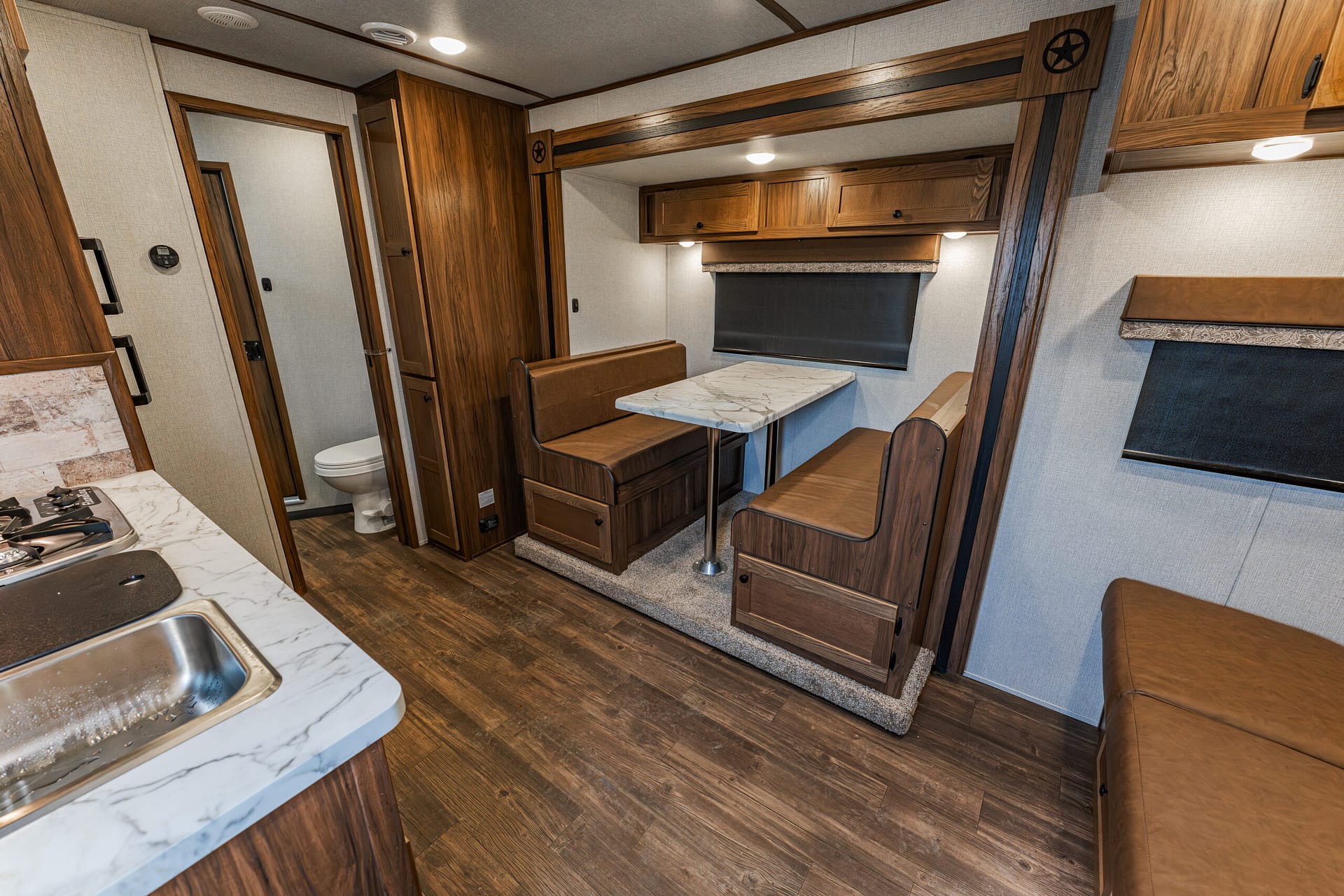 Cozy RV interior with a dinette booth and marble table, wood cabinets, and a kitchen counter with a sink.