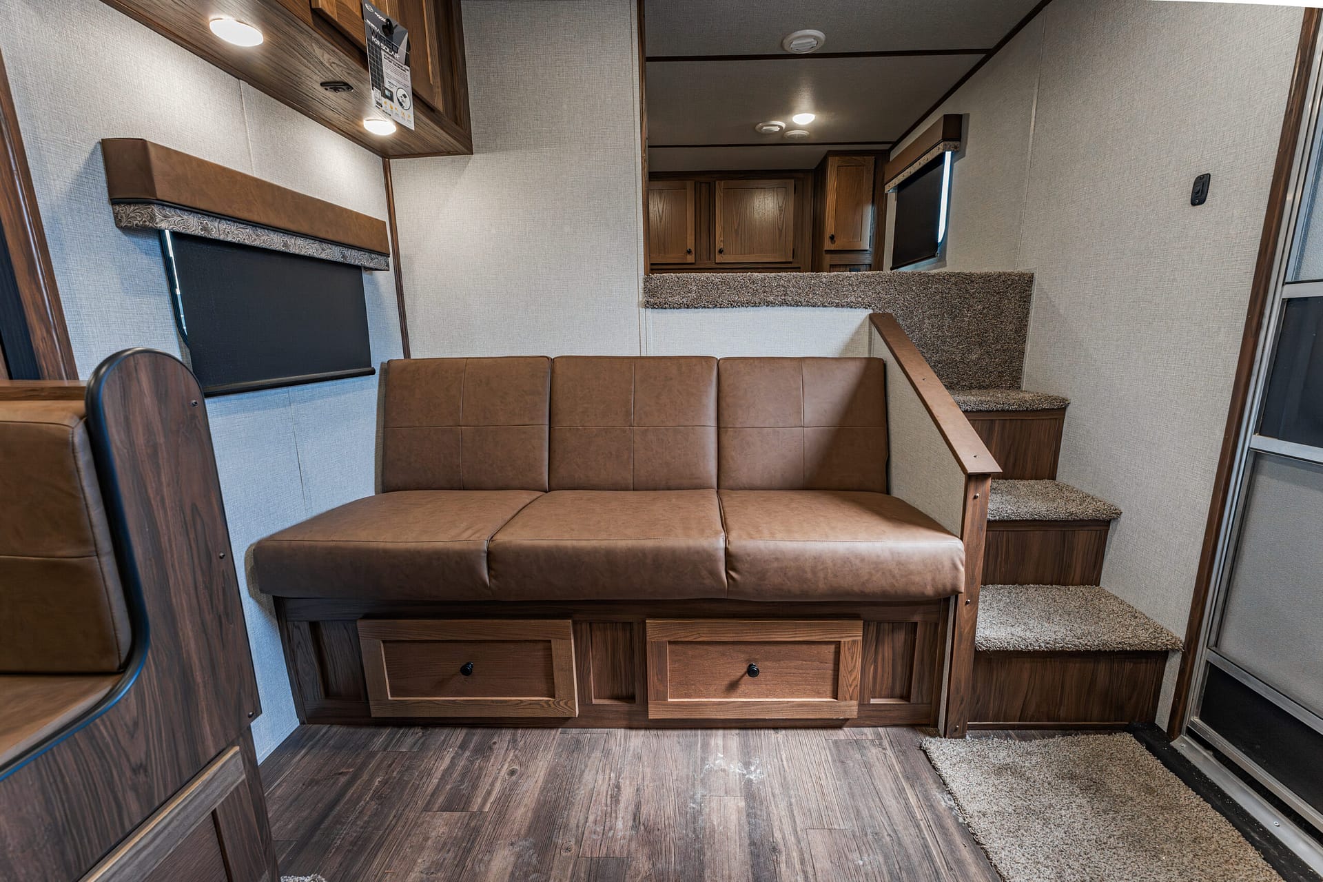 Brown leather sofa with two storage drawers underneath sits in a compact RV living area with wood cabinets nearby.