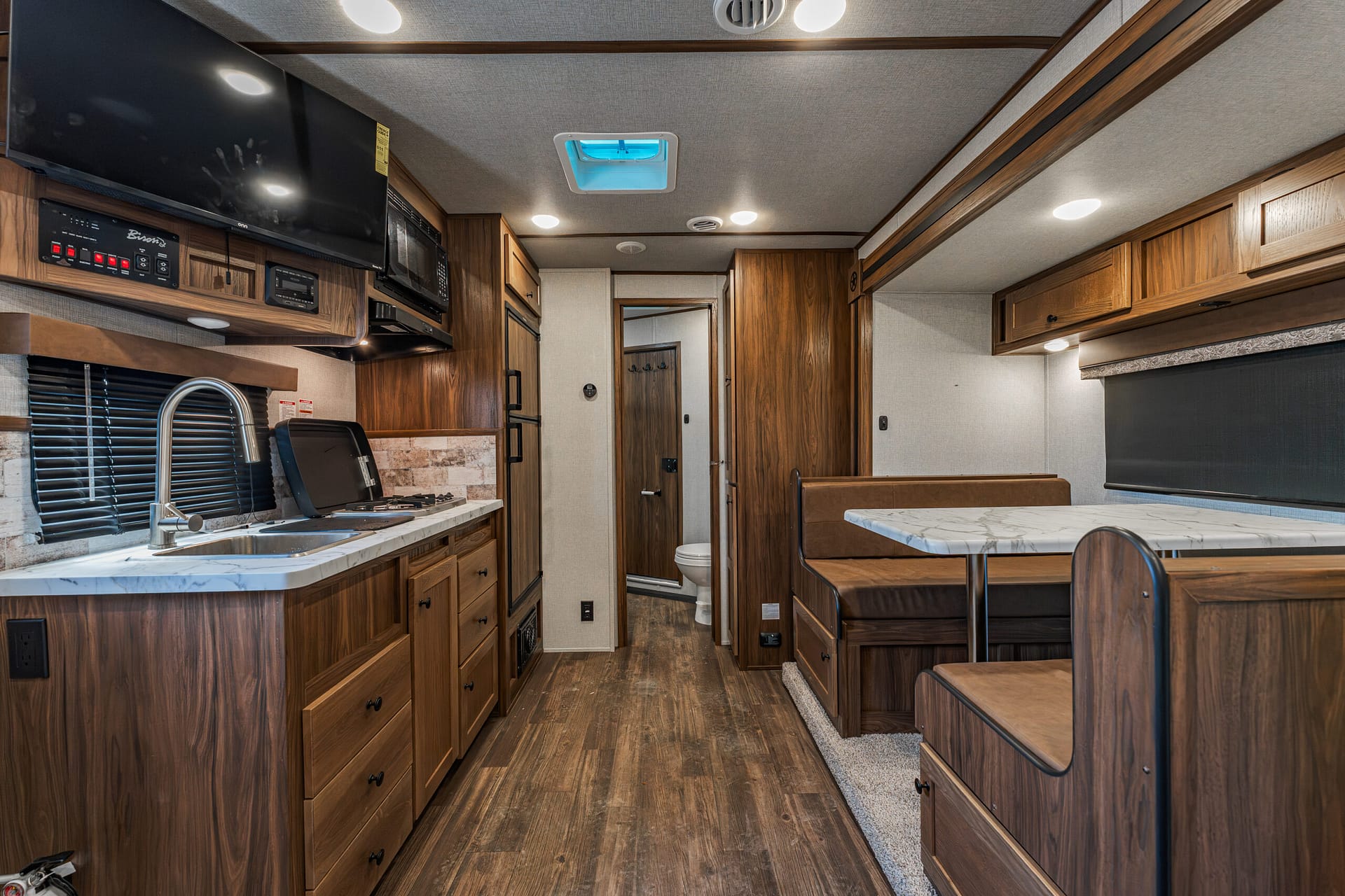RV kitchen with wood cabinets, marble countertop, stainless sink, stove and microwave, plus a booth dinette.