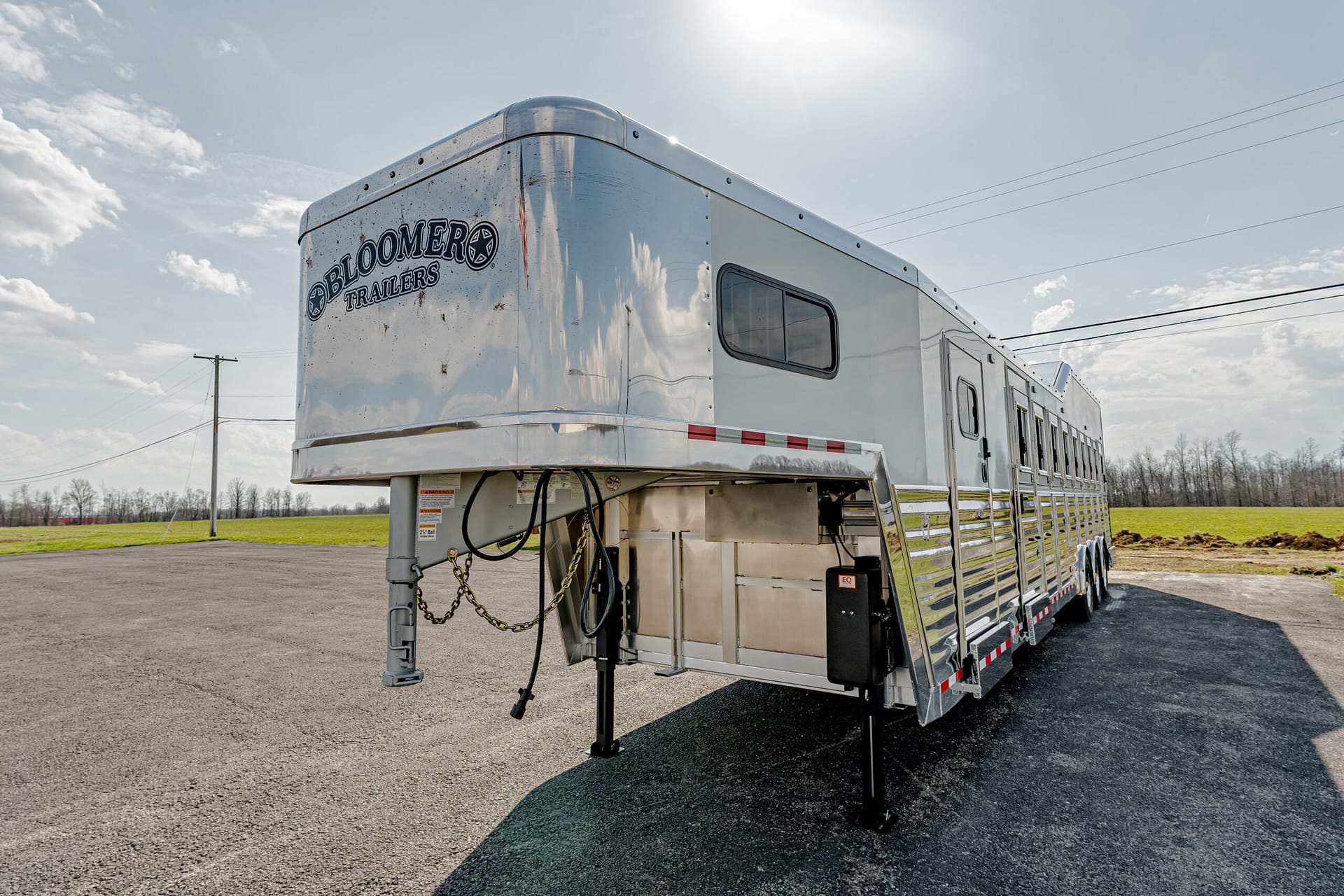 Shiny Bloomer horse trailer on a paved lot, with a grassy field and power lines in the background.