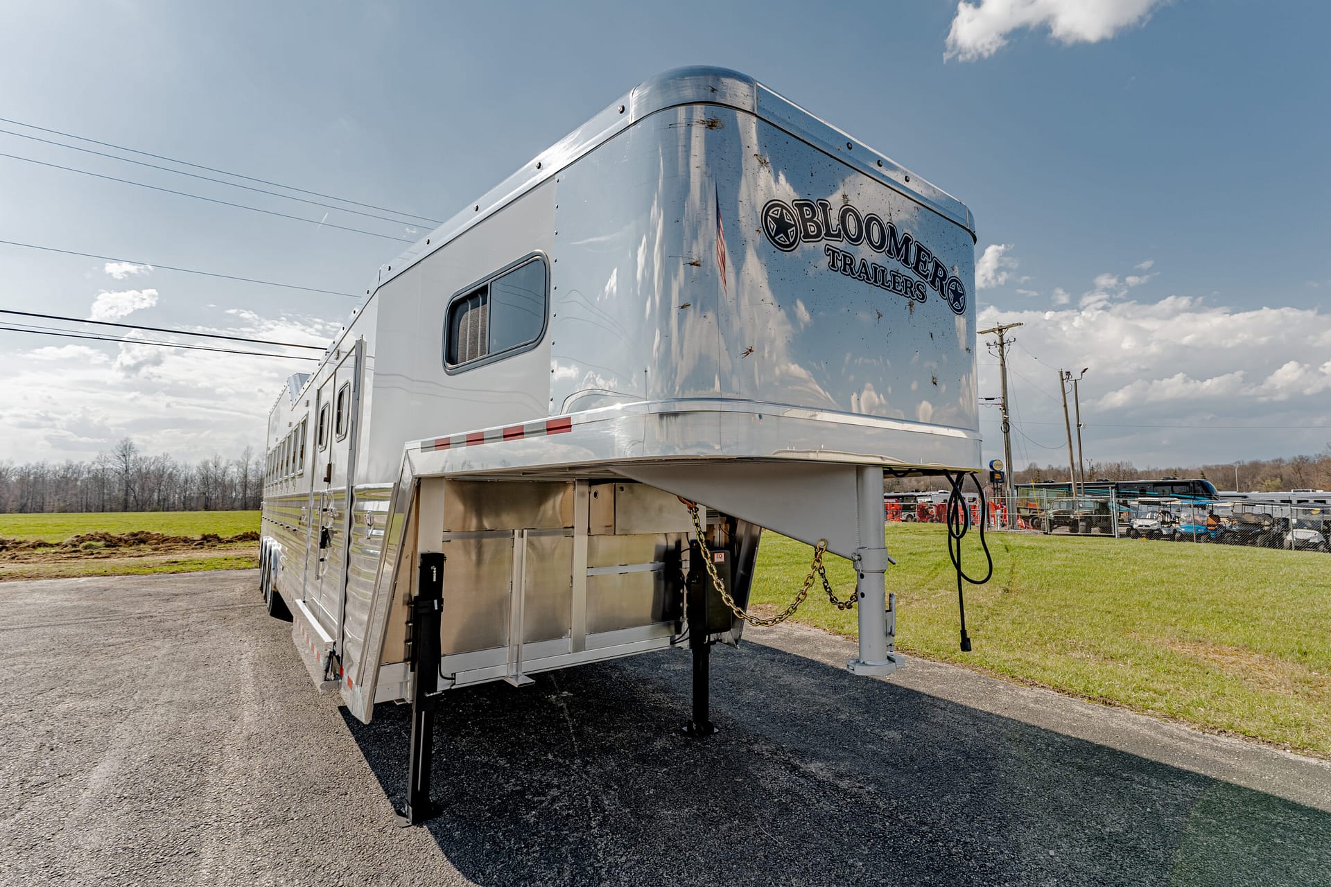 Polished aluminum gooseneck horse trailer on a paved lot with the Bloomers Trailers logo on the front corner.