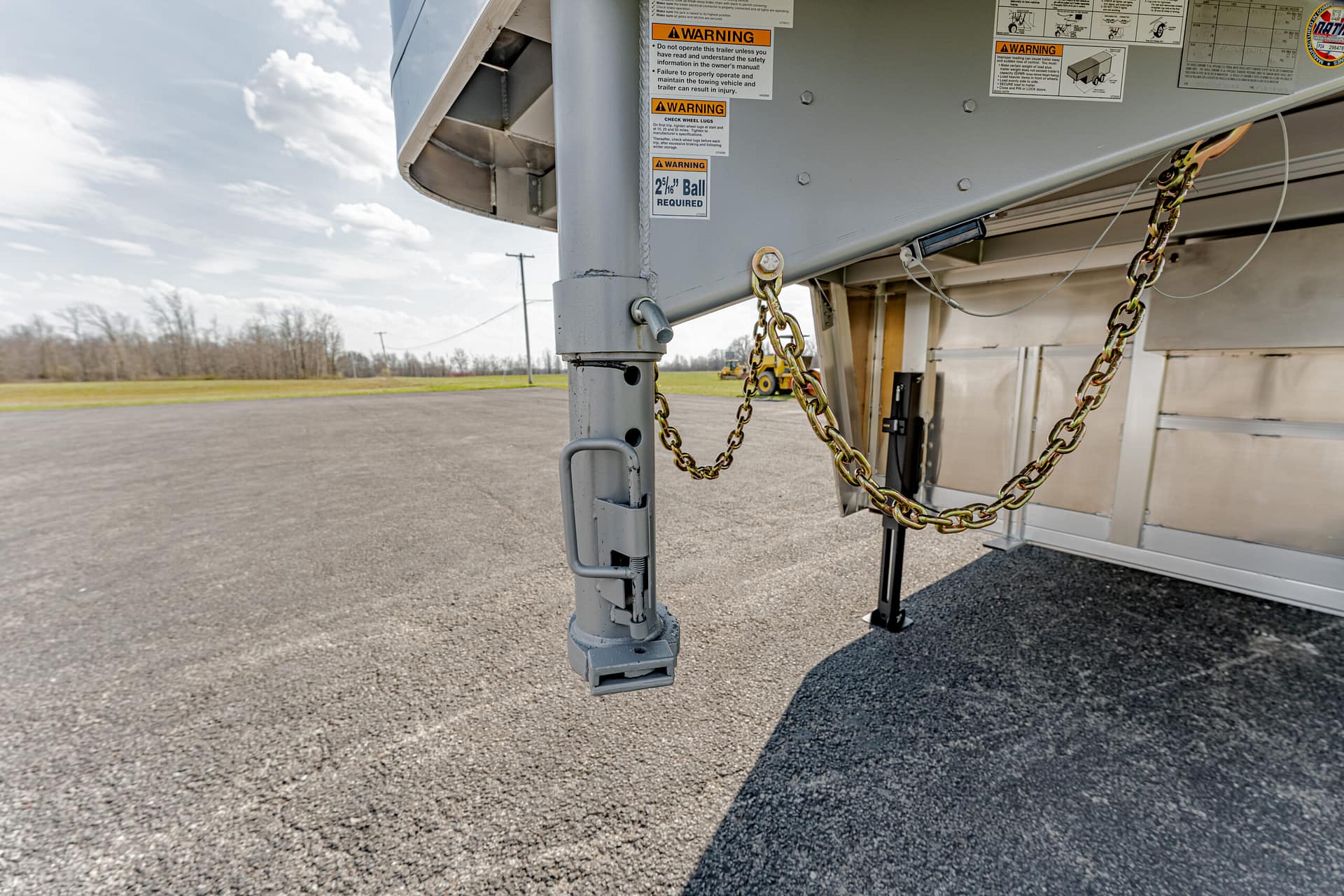 Close-up of a trailer’s landing gear and safety chains hanging from a gray semi-trailer on an asphalt lot.