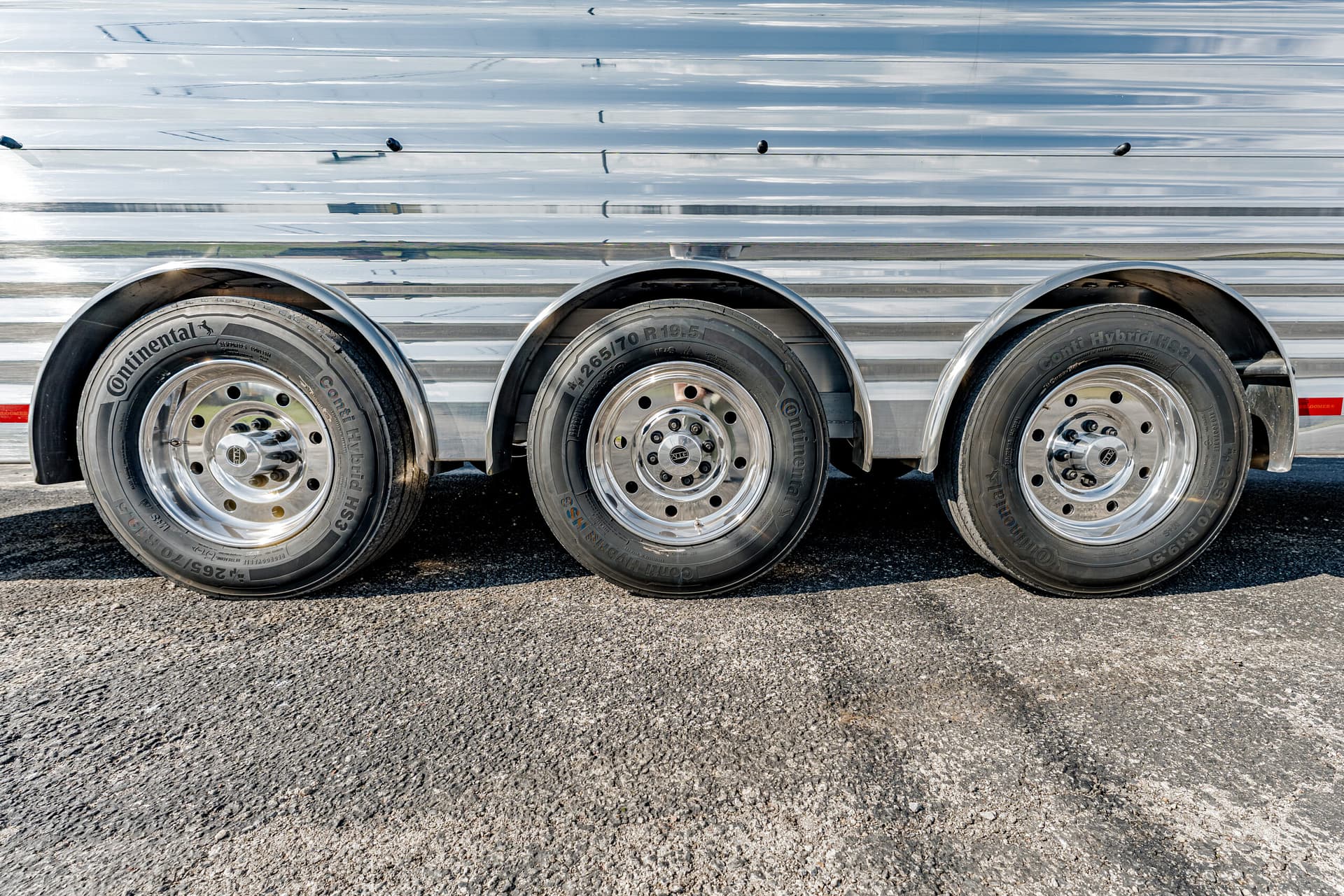 Triple-axle trailer with polished steel wheels and Continental tires on an asphalt surface