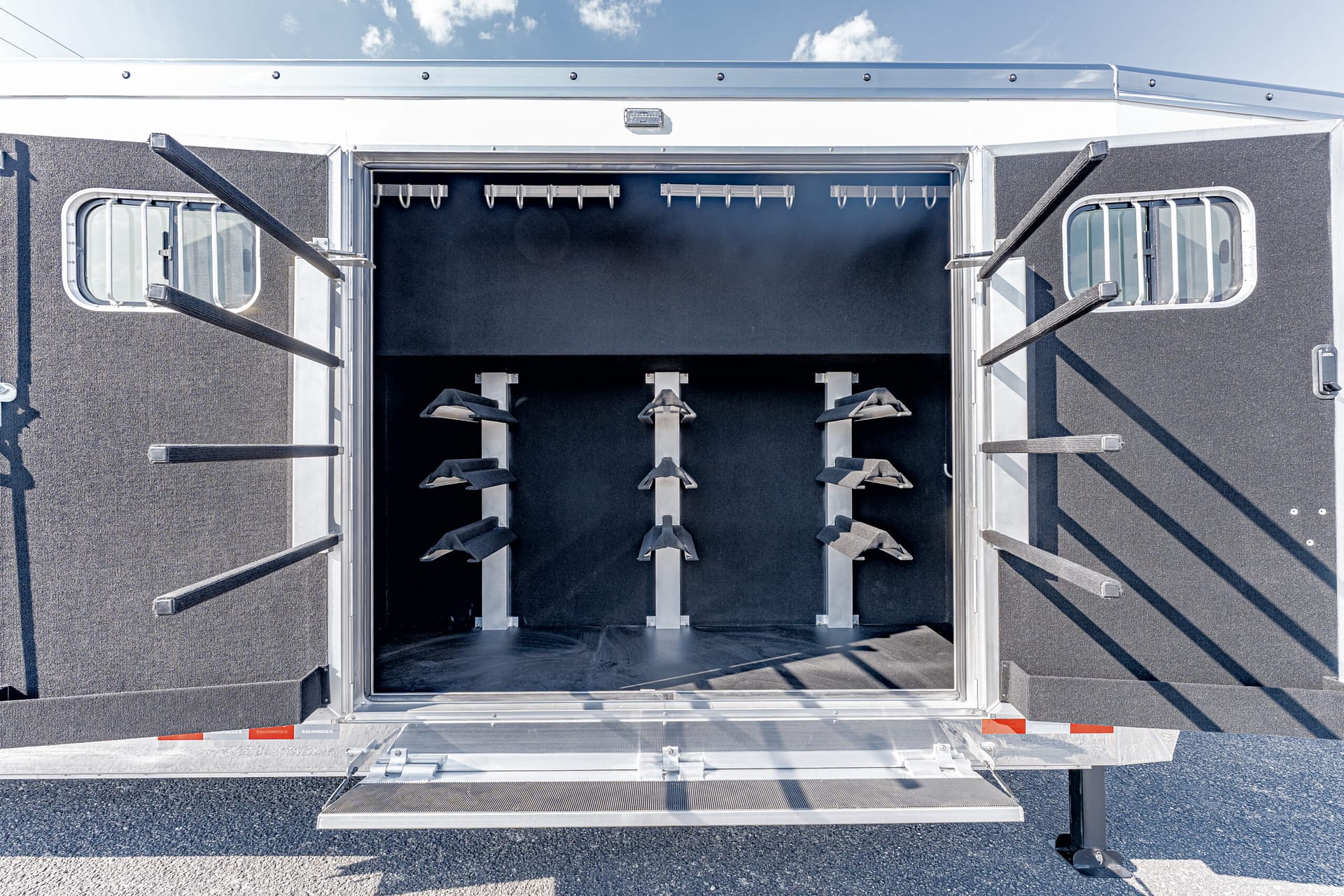 Open horse trailer showing interior tack area with vertical saddle racks along the walls and hooks at the top edge of the ceiling area.