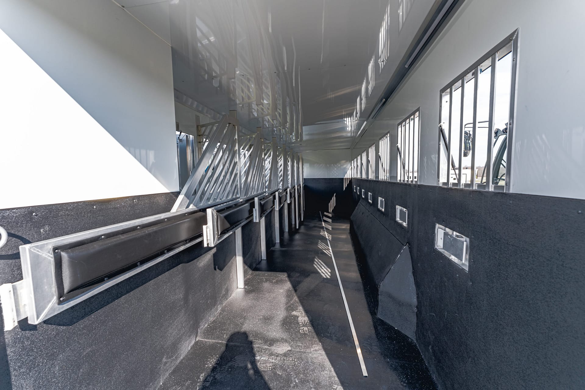 Interior of an empty trailer with black lower walls, metal tie‑down rails, and windows along the right side letting light in.