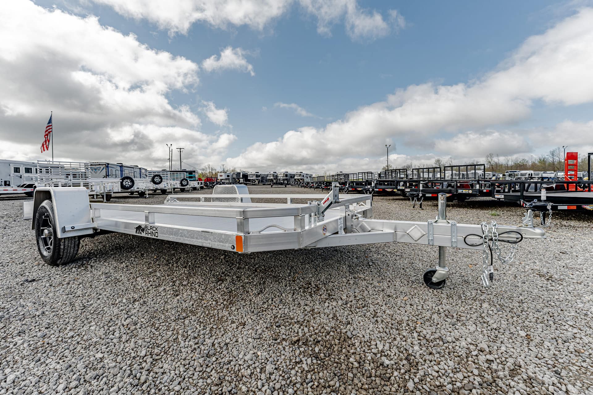 Row of flatbed trailers parked on a gravel lot with an American flag in the distance.