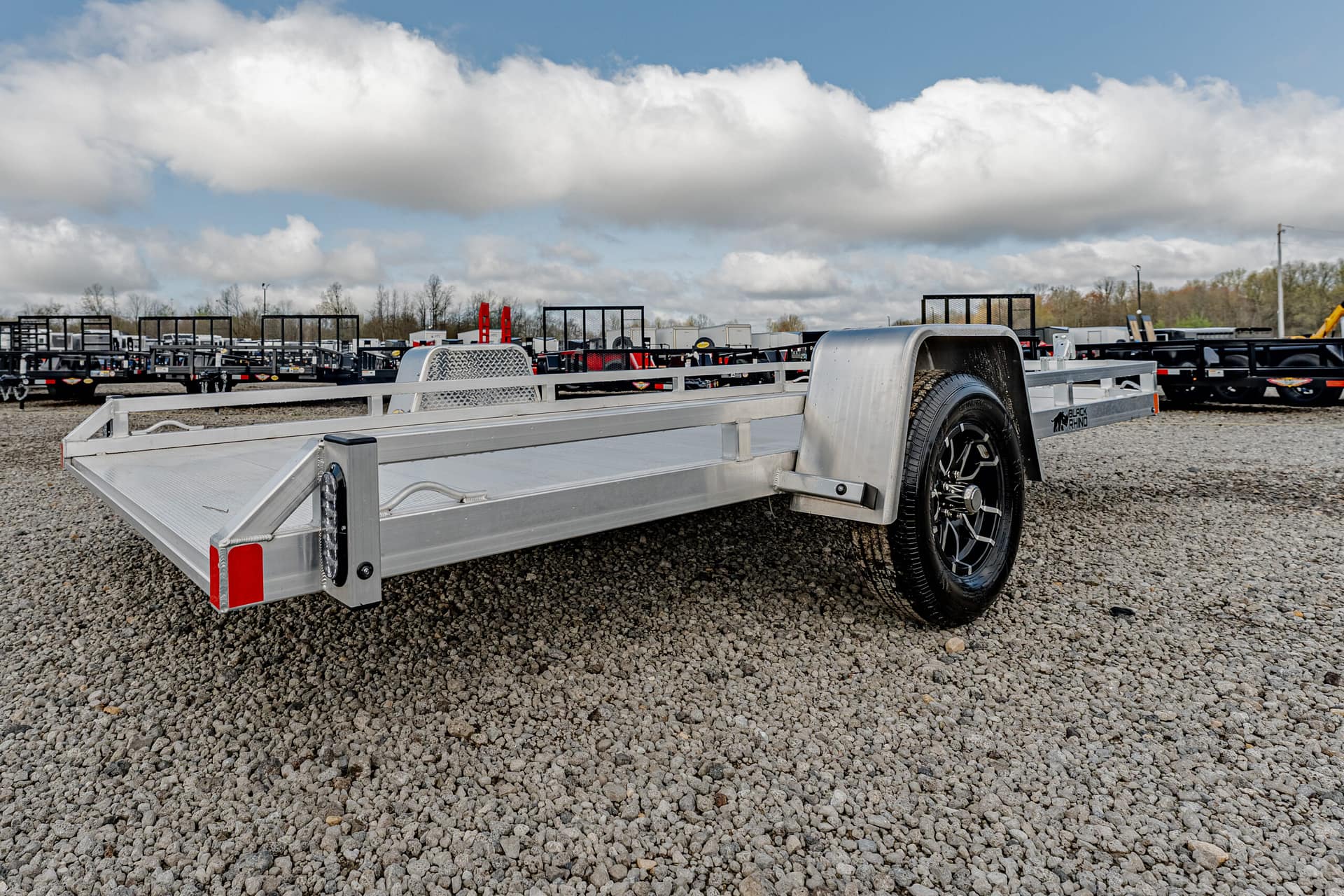 Aluminum trailer on a gravel lot with rows of trailers in the background and a cloudy sky above.
