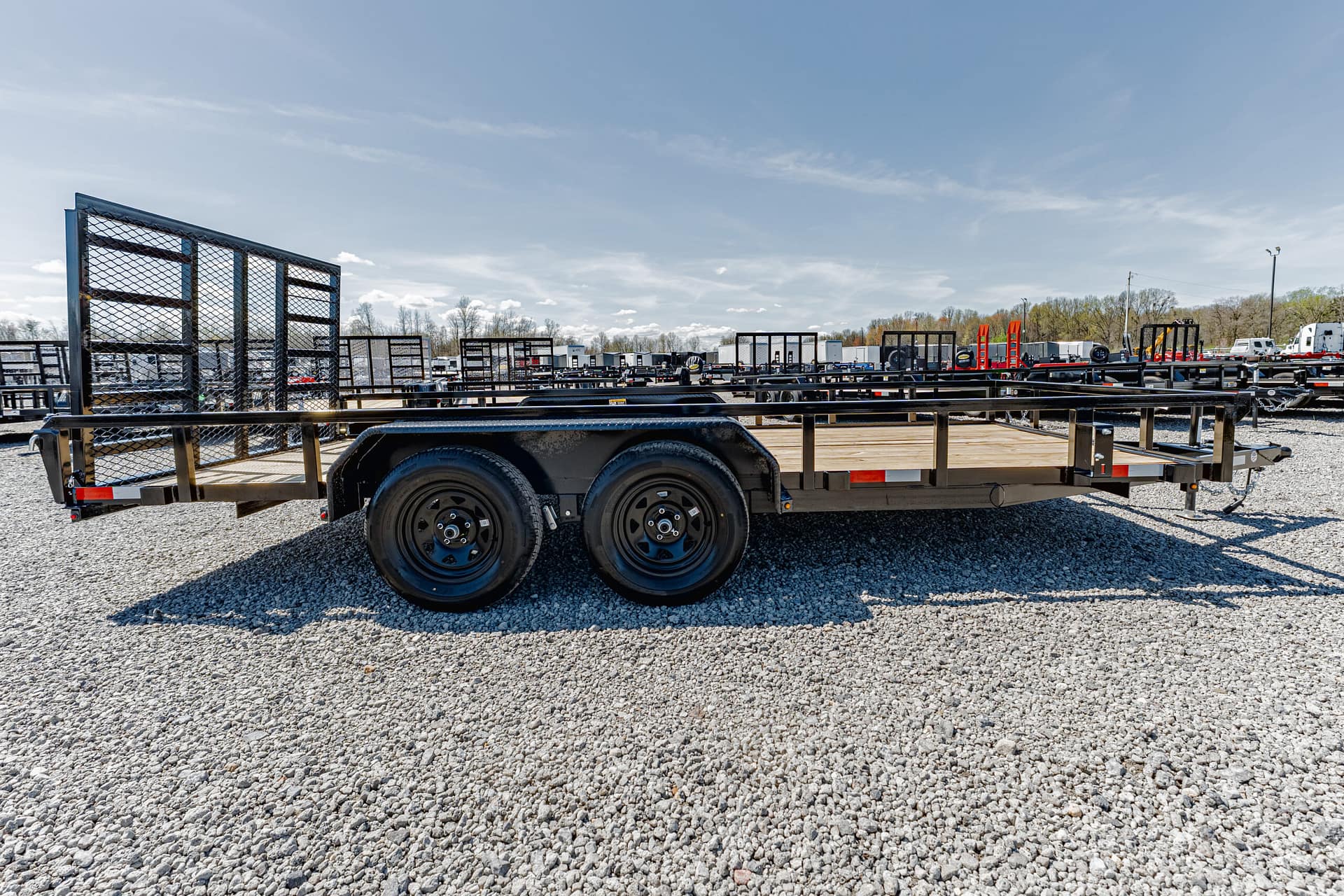 Wide view of a gravel lot filled with flatbed trailers and racks under a clear blue sky.