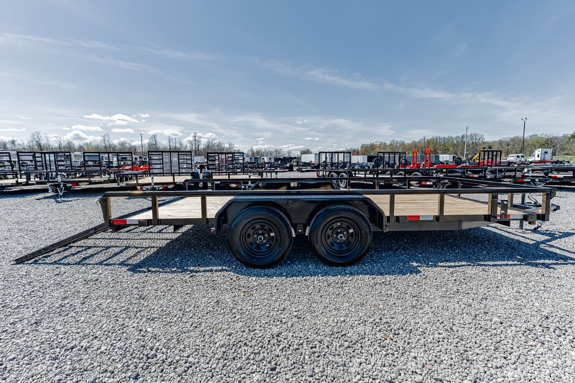 Row of flatbed trailers parked in a gravel lot under a clear blue sky