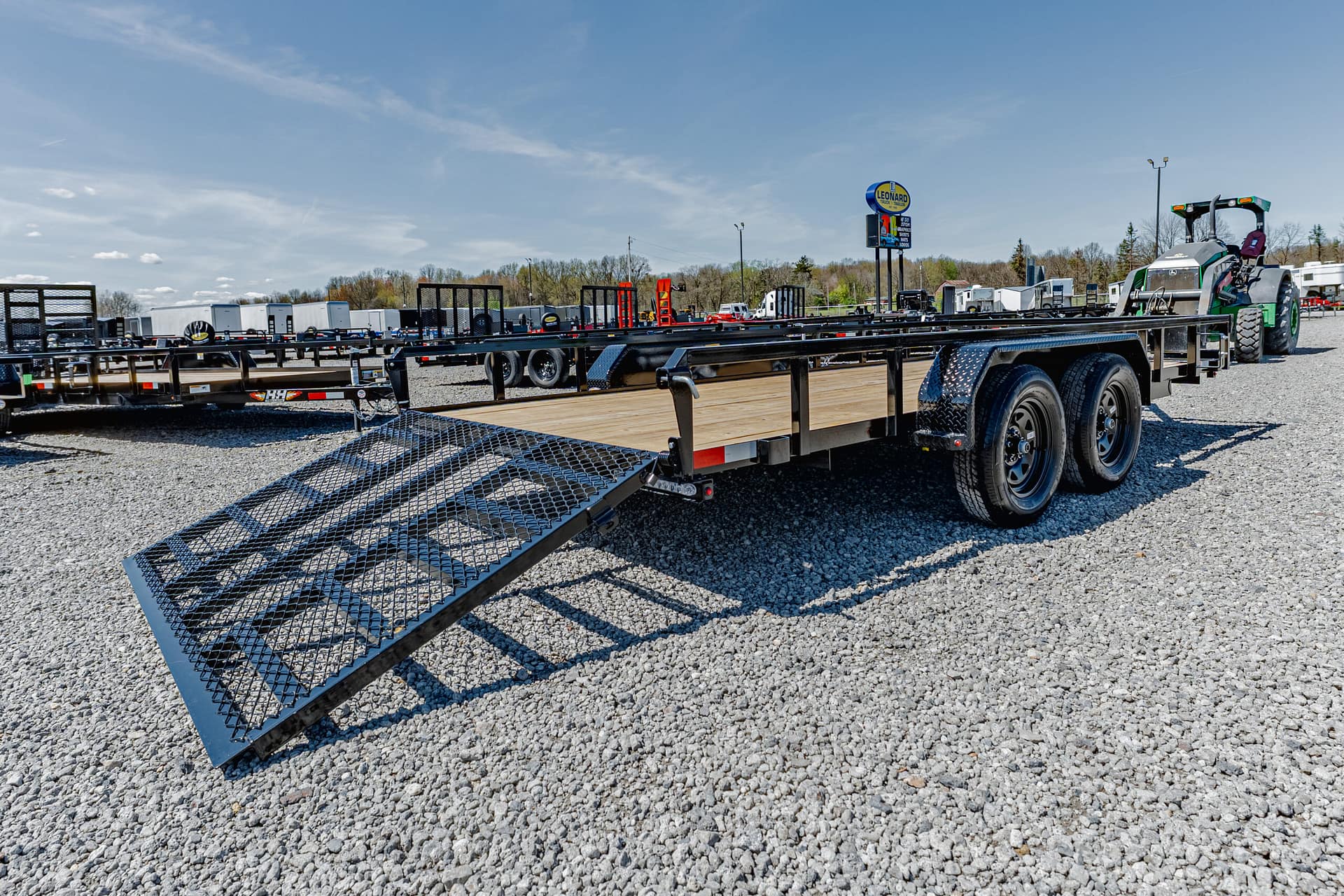 Wide view of a trailer yard with multiple flatbed trailers on gravel under a clear blue sky