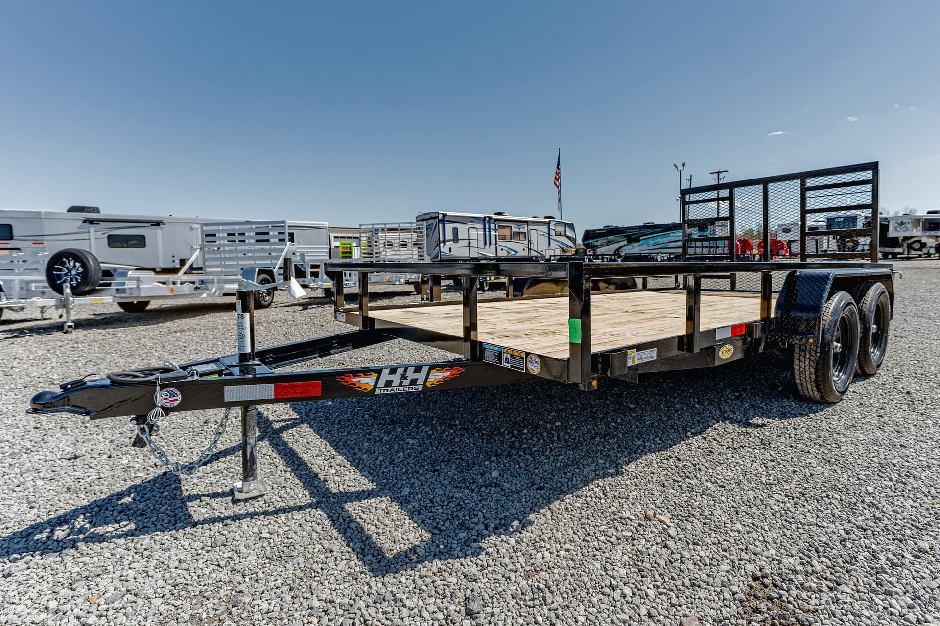 Black utility trailer on a gravel lot with other trailers and RVs in the background under a clear blue sky