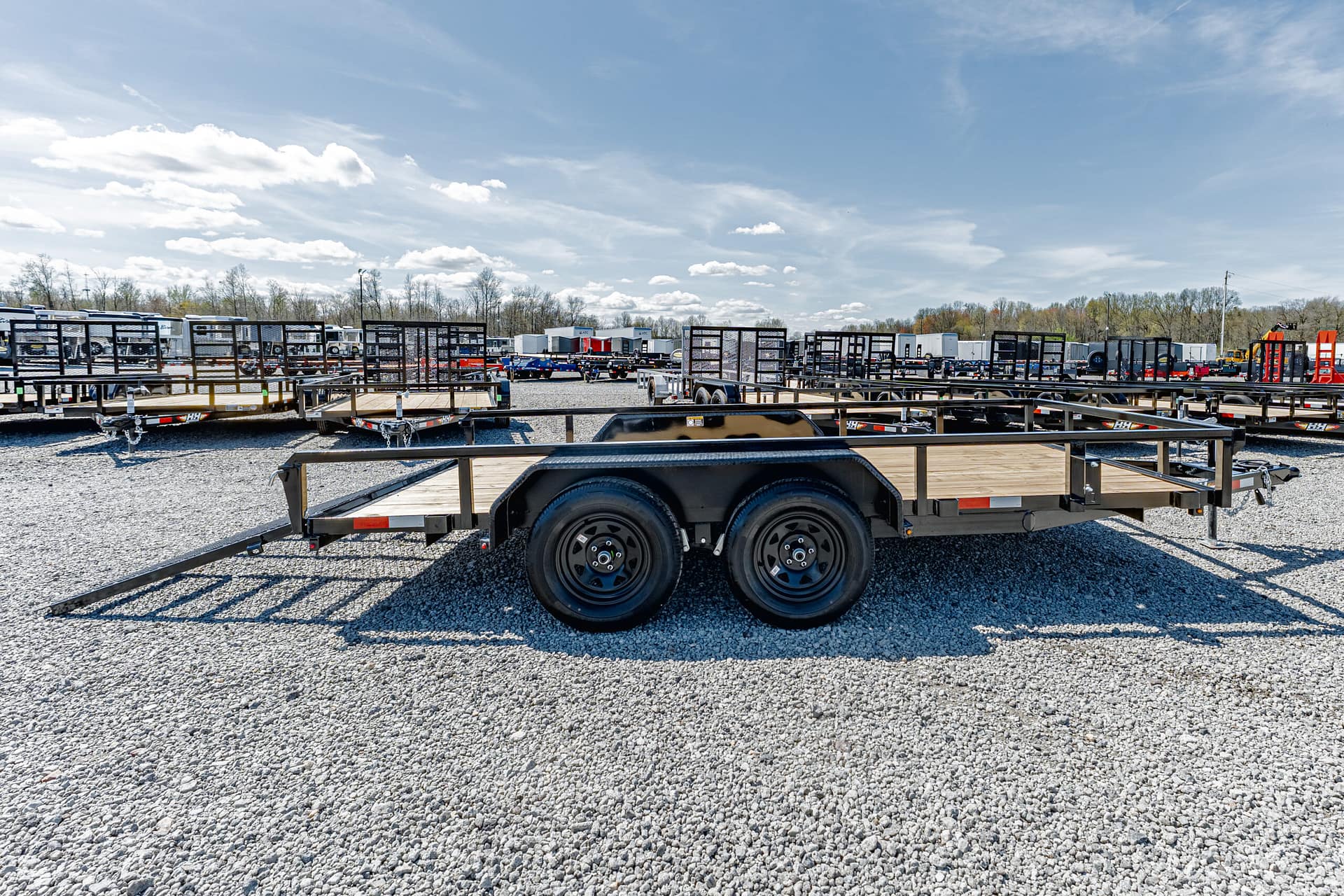Row of flatbed trailers parked in a gravel lot under a blue sky.