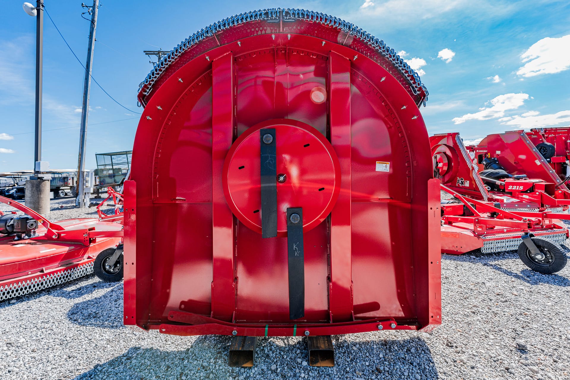 Rear view of a red round baler in a gravel lot, showing the large circular bale chamber and metal framework outside the machine edge.