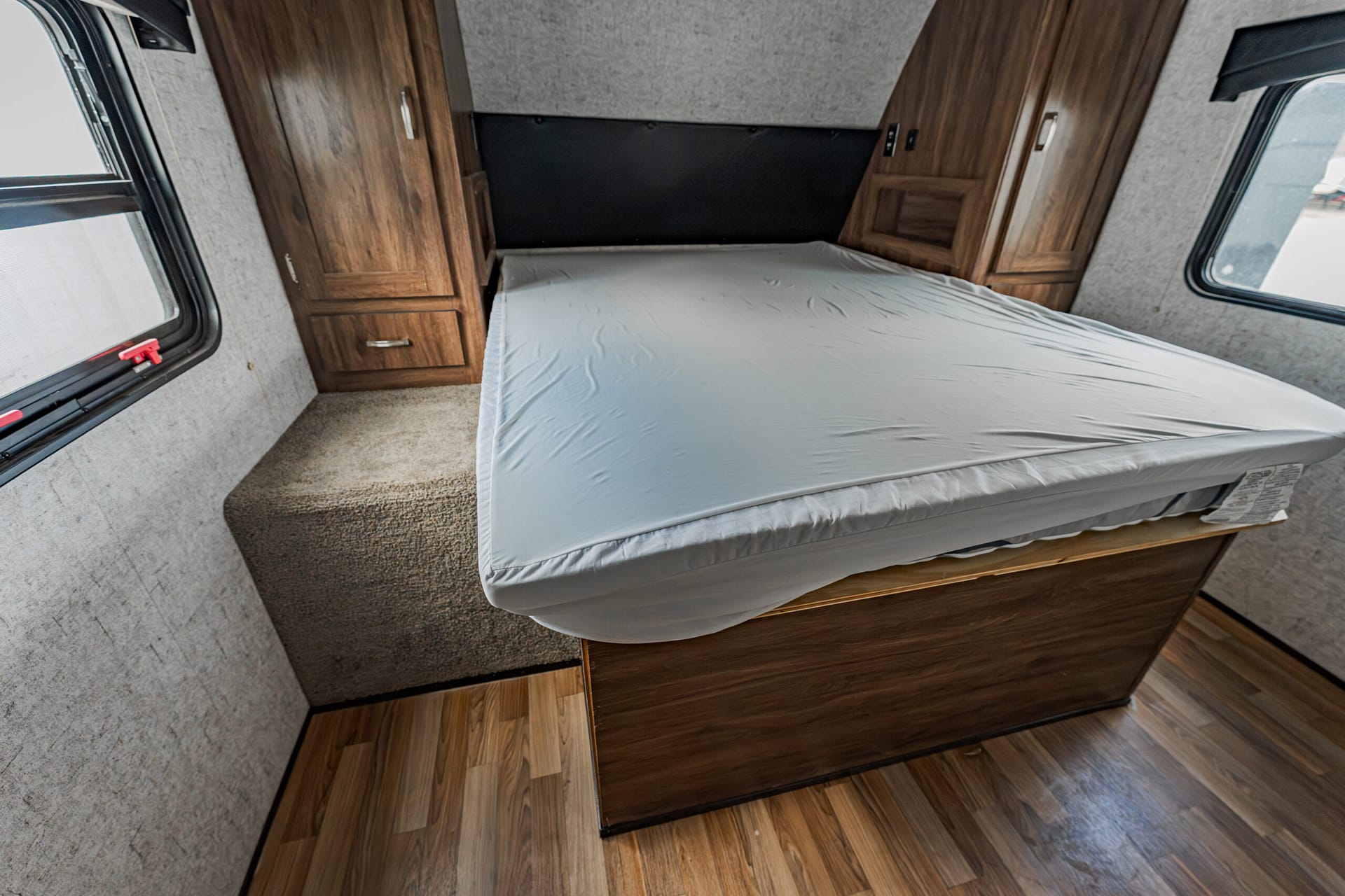 Interior of a travel trailer bedroom with a full bed, wood cabinets along the walls, and windows on both sides.