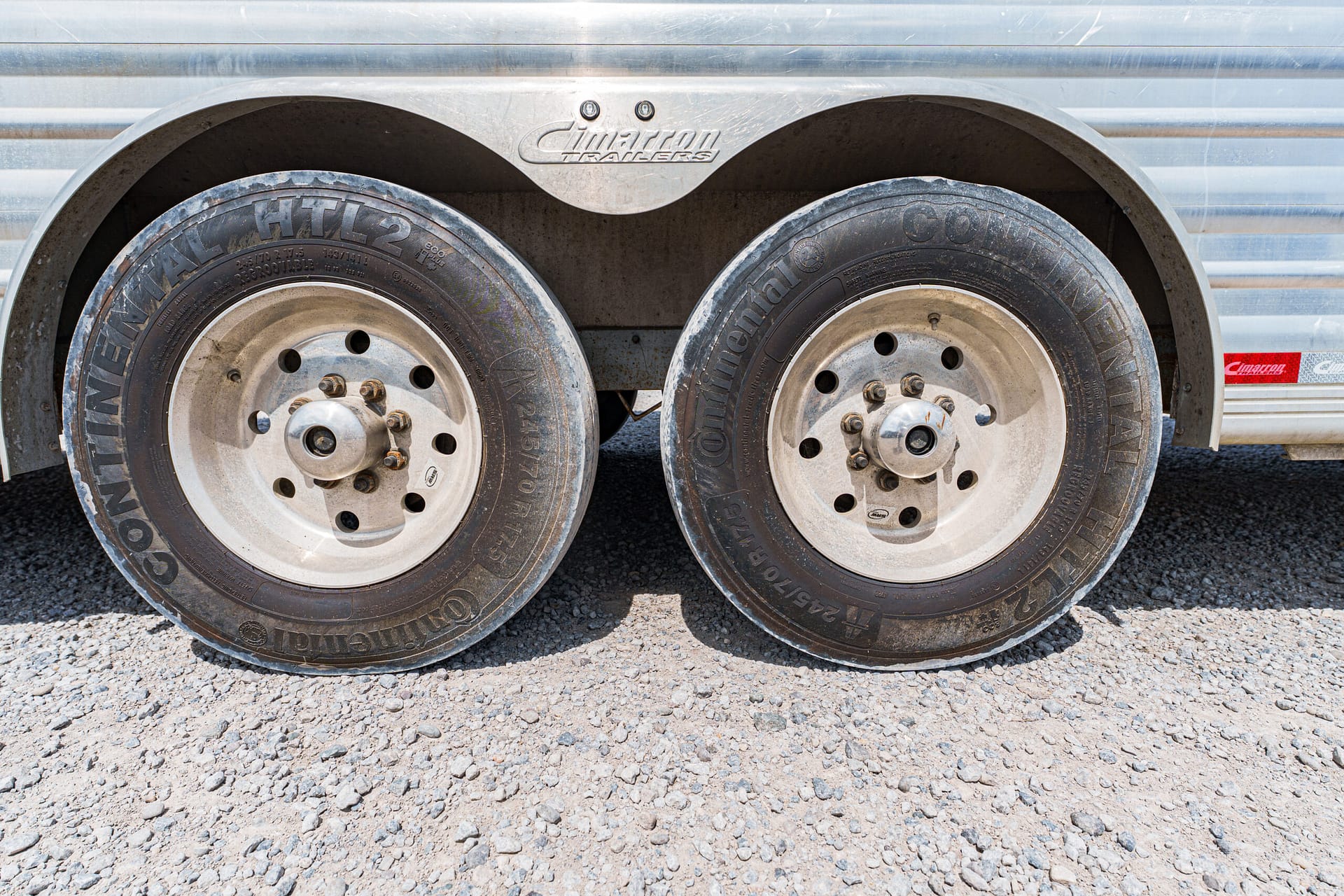 Close-up of tandem trailer wheels and a metal fender with the Cimarron Trailers logo on the trailer body