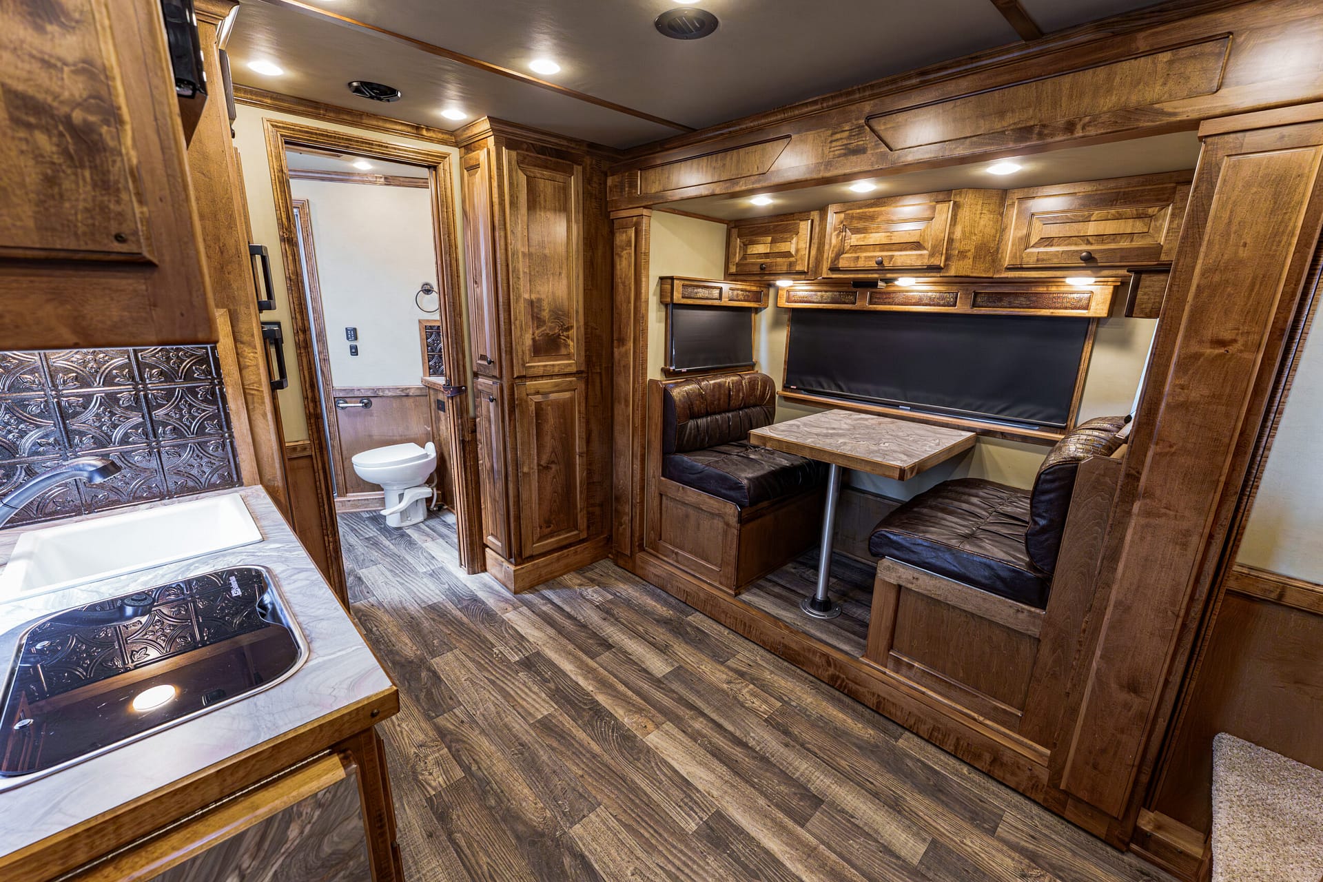 Wood-paneled RV interior with a dinette, marble-like table, and upper cabinets; a small bathroom door is visible to the left.
