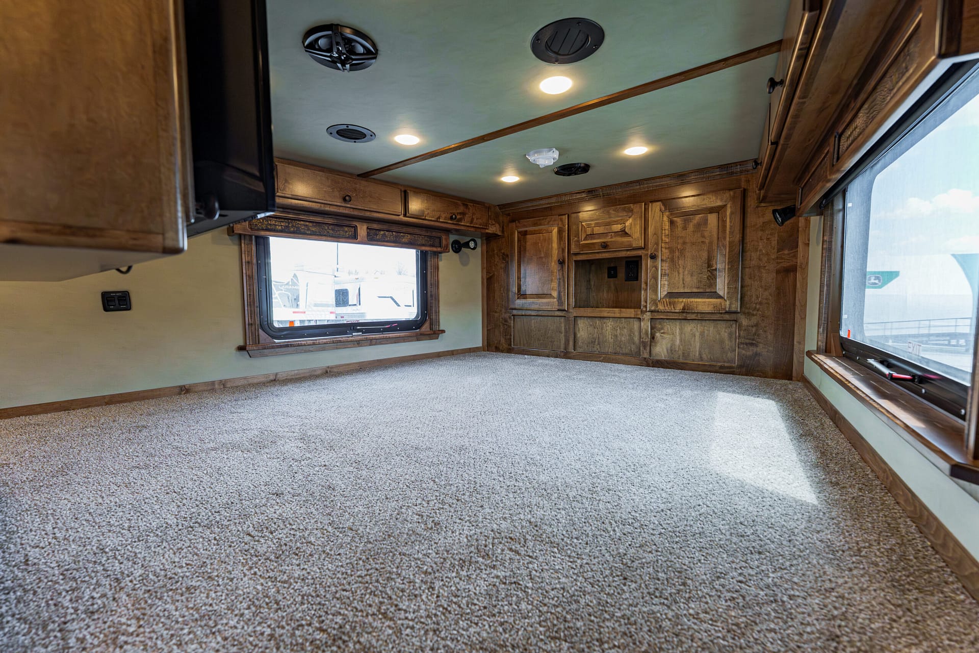 Cozy RV interior with dark wood cabinets, large windows, and a carpeted floor.