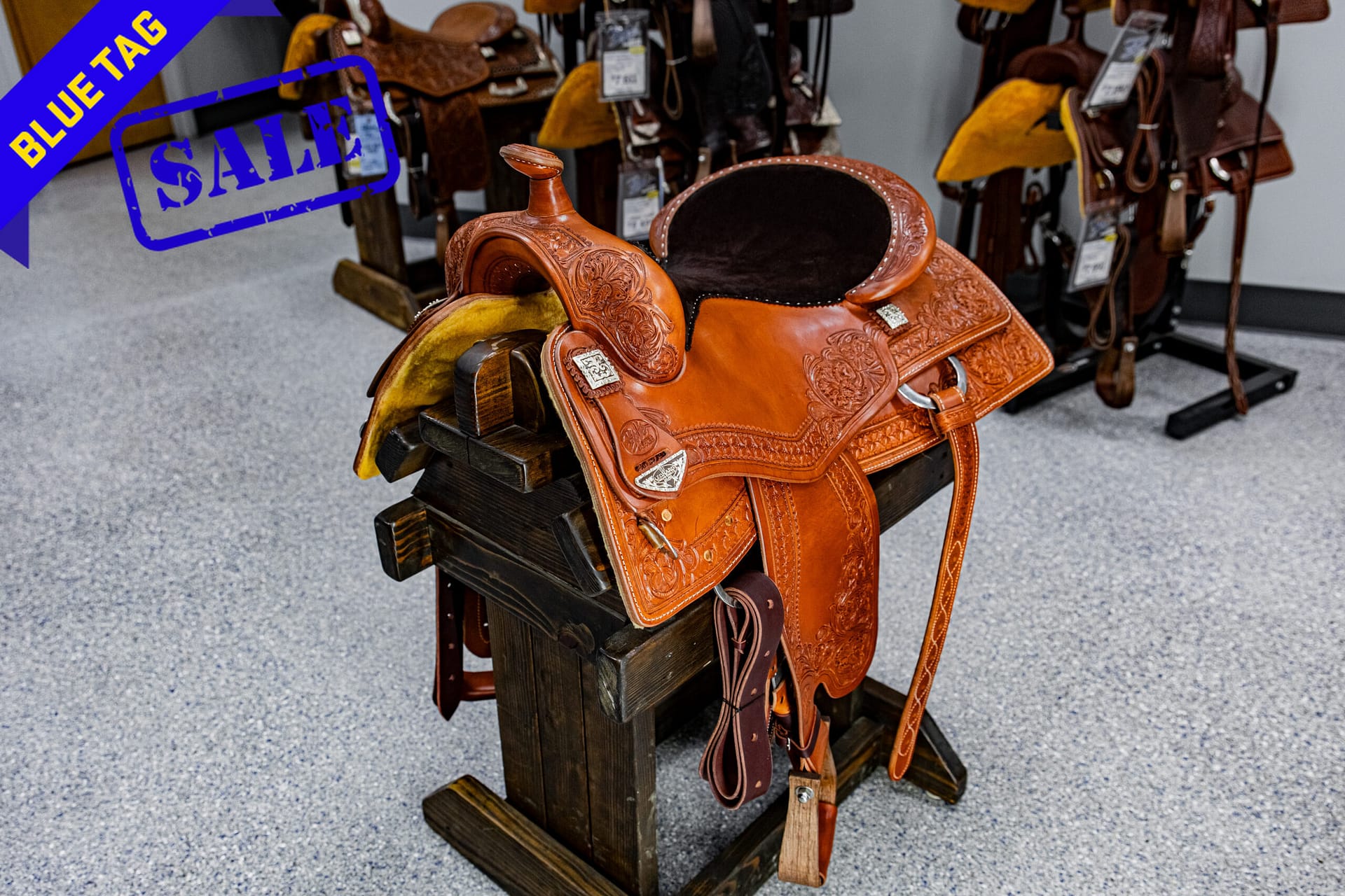 Leather western saddle on a display rack with a blue 'Blue Tag' sale banner in the corner.