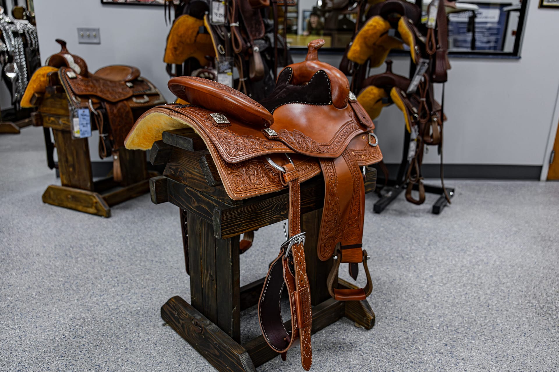 Leather Western saddles on display in a tack shop, ornate tooling and brown tones visible.