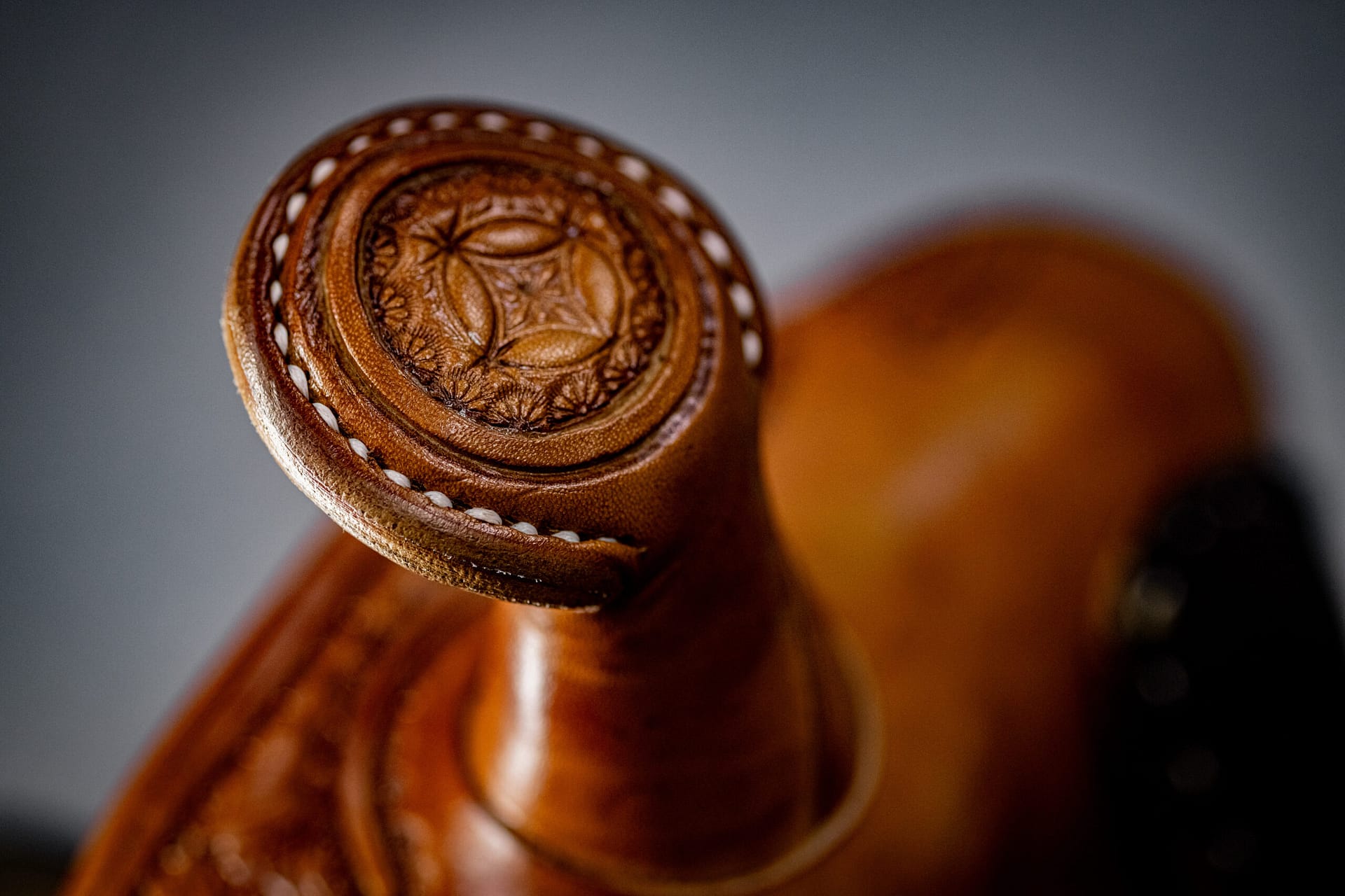 Close-up of a brown leather cowboy boot showcasing a carved floral and geometric pattern on the heel with white stitching along the edge.
