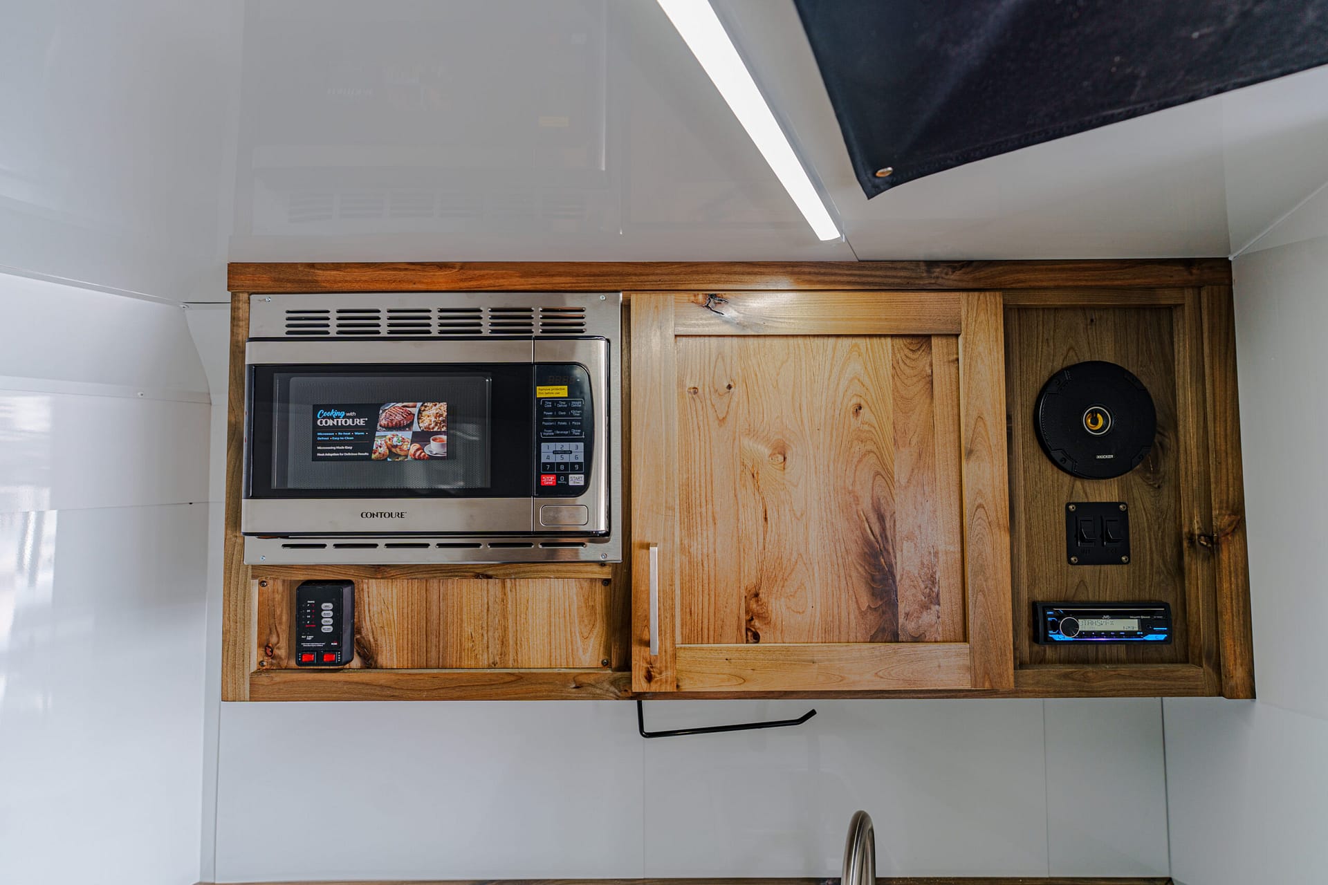 Wooden kitchen cabinets with a built-in stainless microwave and a black round speaker on the right wall inside a compact space.