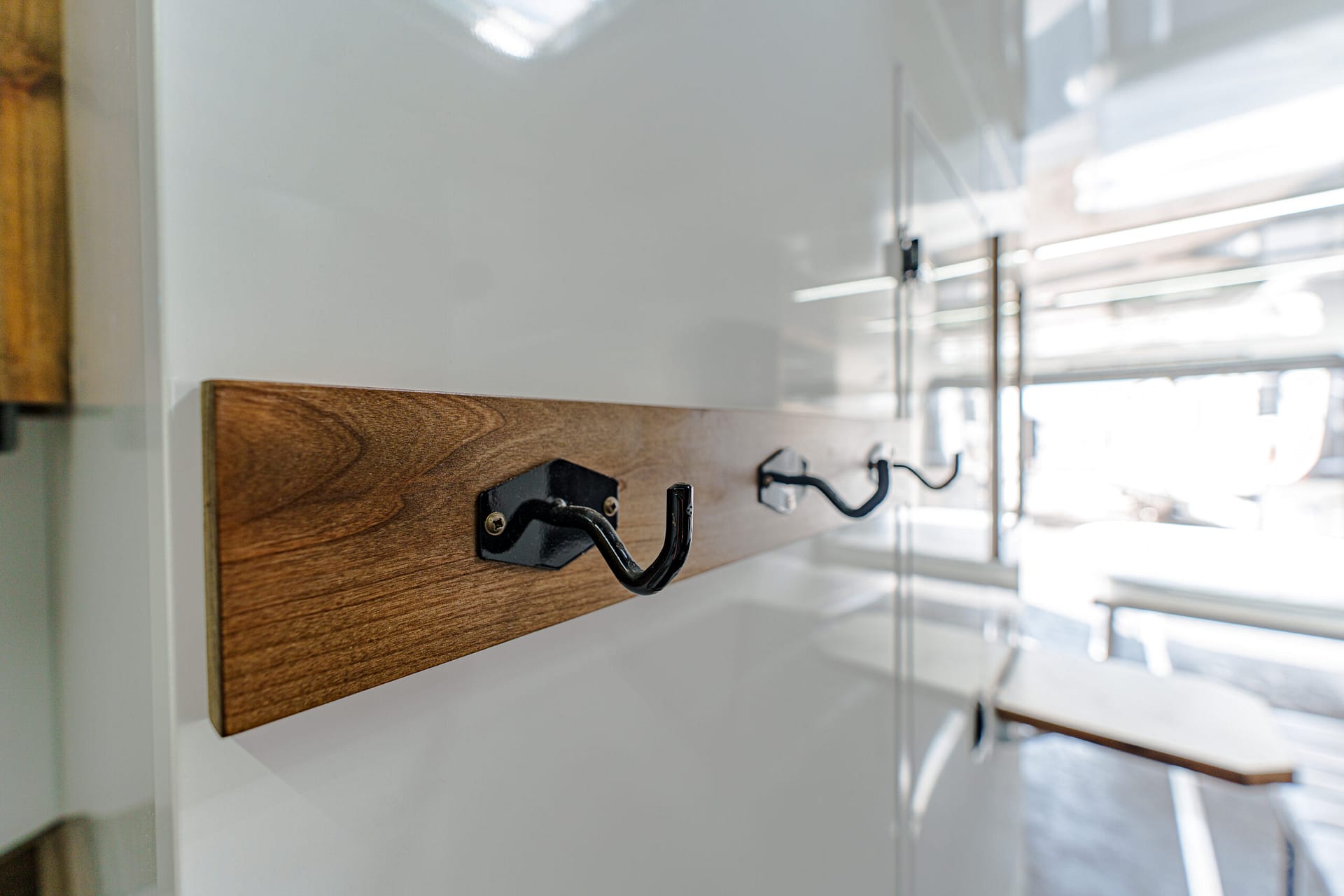 Wooden rail with two black curved hooks mounted on a white cabinet, in a bright kitchen area.
