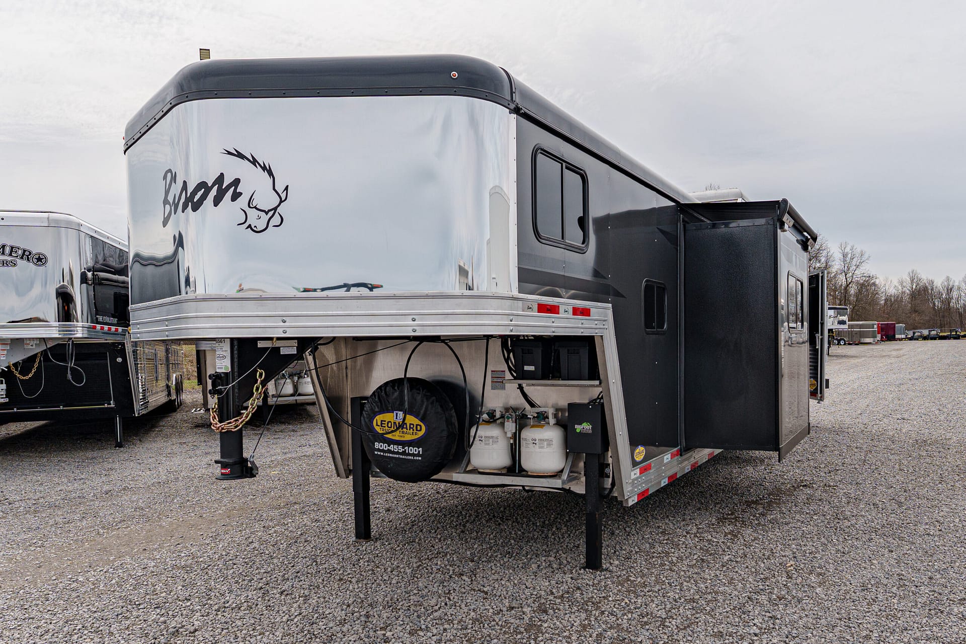 Silver gooseneck trailer with a black buffalo graphic on the front, parked on a gravel lot with other trailers nearby.