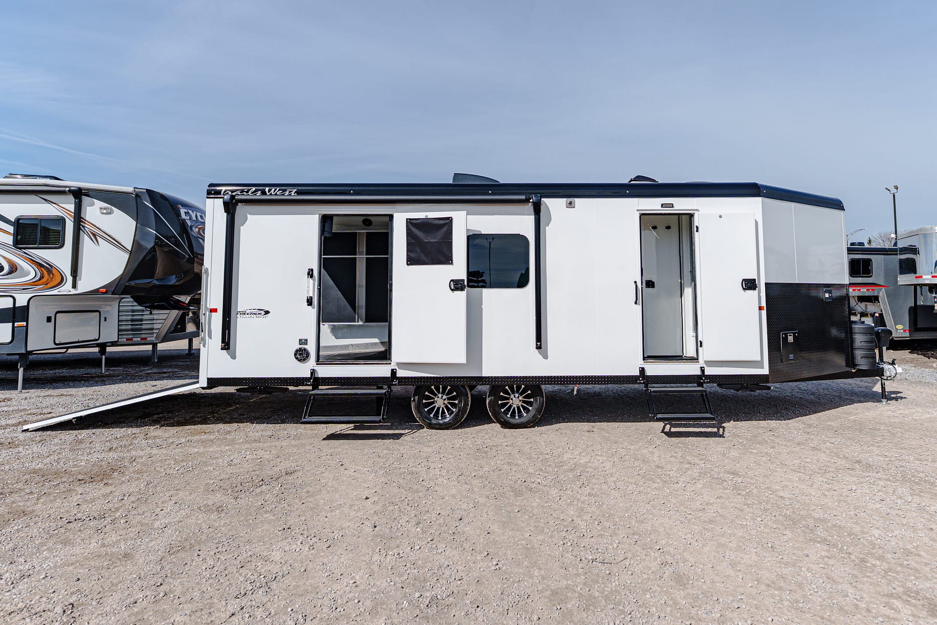 Row of white travel trailers parked on a gravel lot under a clear blue sky.