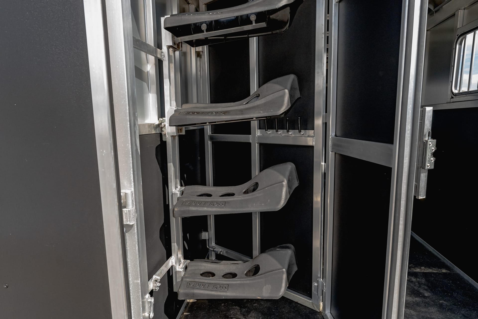 Narrow view of a metal industrial staircase with perforated tread steps inside a dark equipment cabinet; gray rails and supports visible on both sides, labeled 'SADDLE BOSS' on the steps.