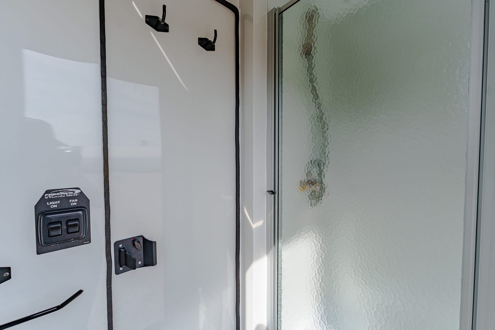 Close-up of a gray wall with a black dual-switch control labeled LIGHT ON and FAN ON, beside a frosted glass door/window.