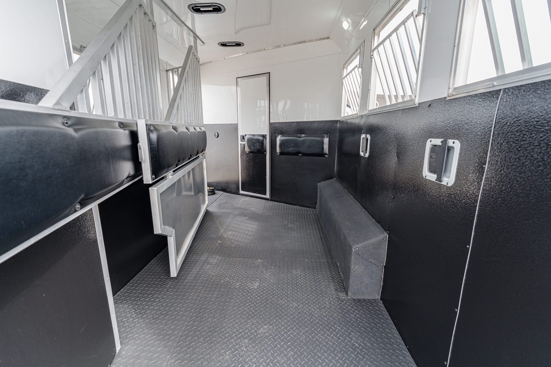Interior of a black-and-silver livestock trailer with metal stalls and diamond-plate floor