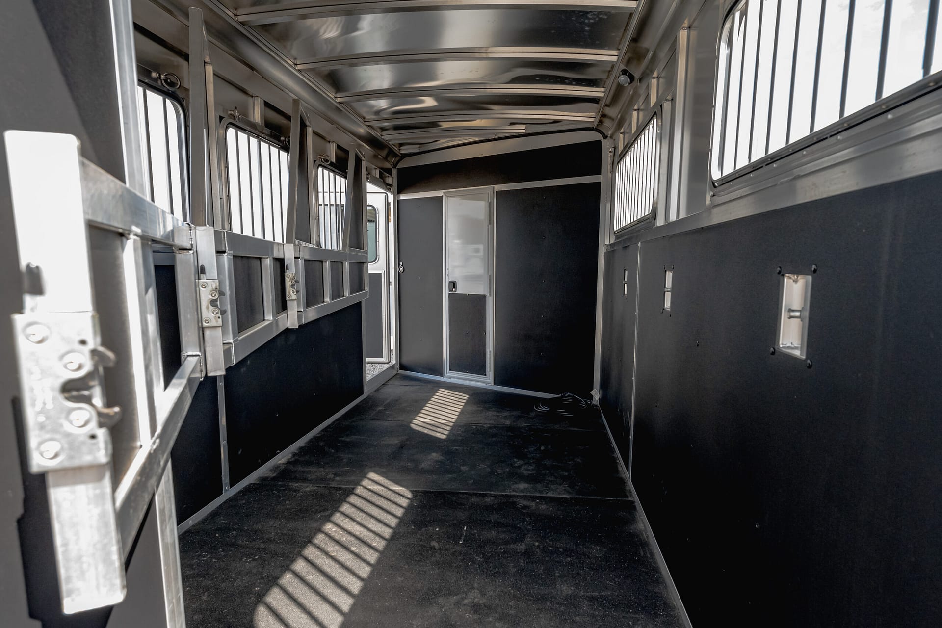 Interior of a metal animal trailer with partitioned stalls along the left wall and a doorway at the far end