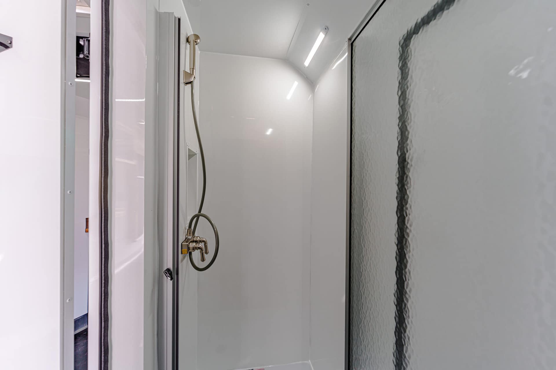 Inside a white, modern shower stall with a handheld showerhead and frosted glass door on the right.