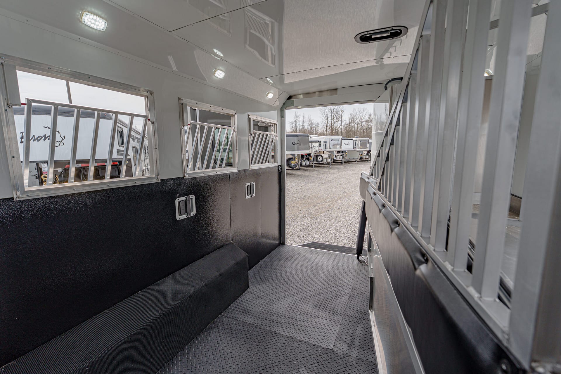 Interior of a trailer with metal dividers, barred windows, and a diamond-plate floor; other trailers are visible outside through the opening.