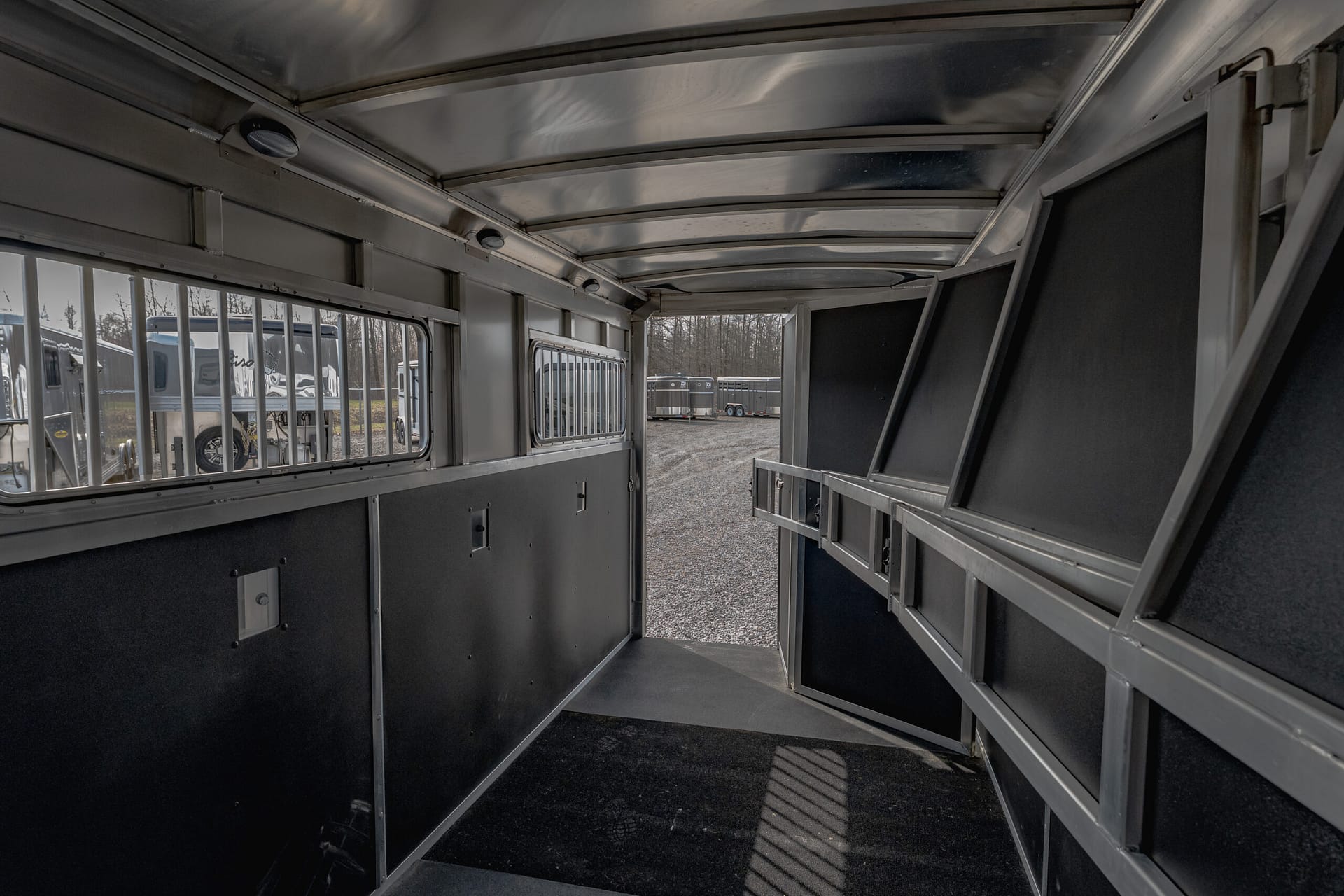 Interior of a metal transport trailer with dark lower walls and barred windows; row of other trailers visible outside through the windows.
