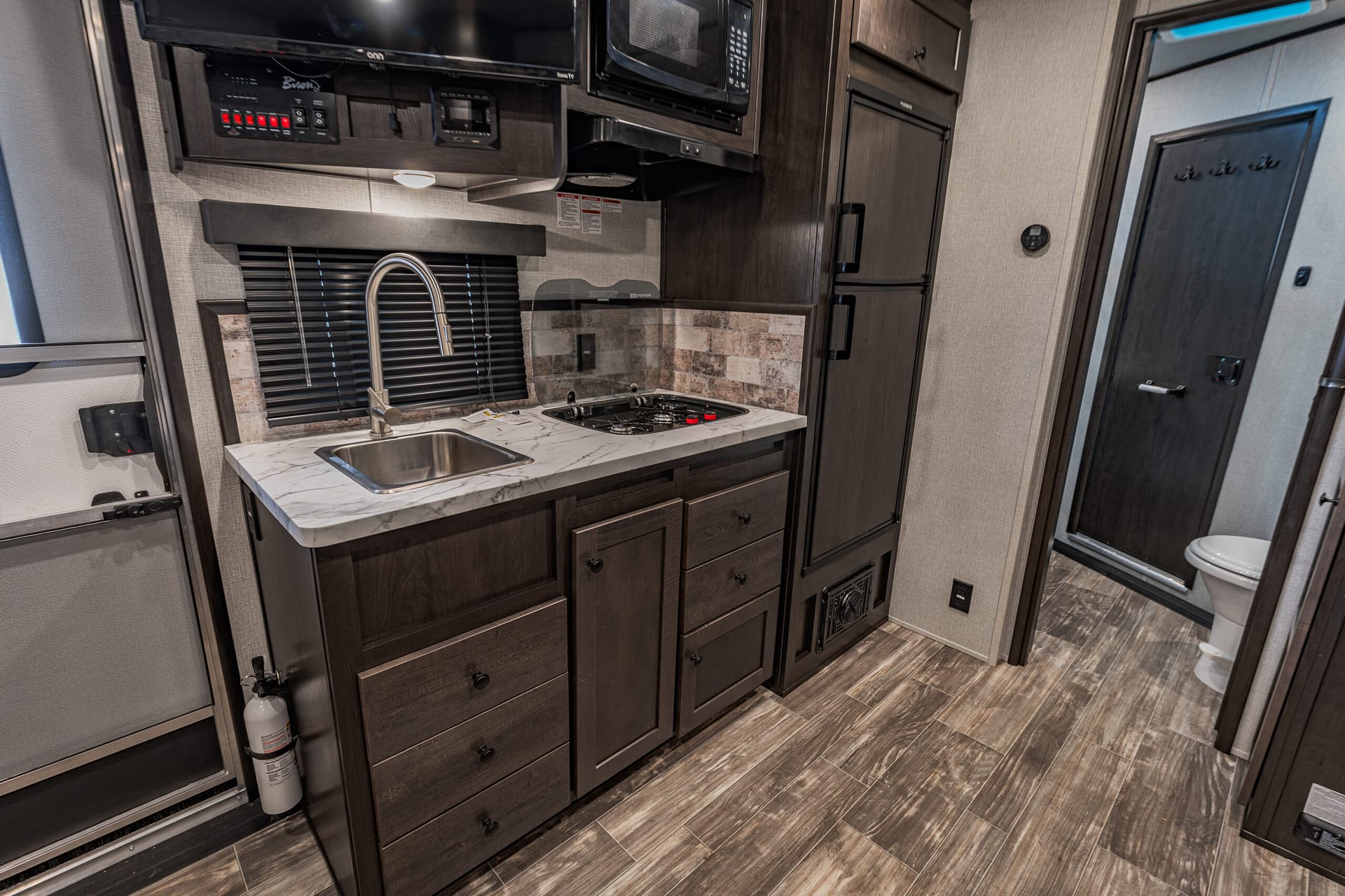 RV kitchen with dark wood cabinets, marble countertop, sink, stove, and microwave.