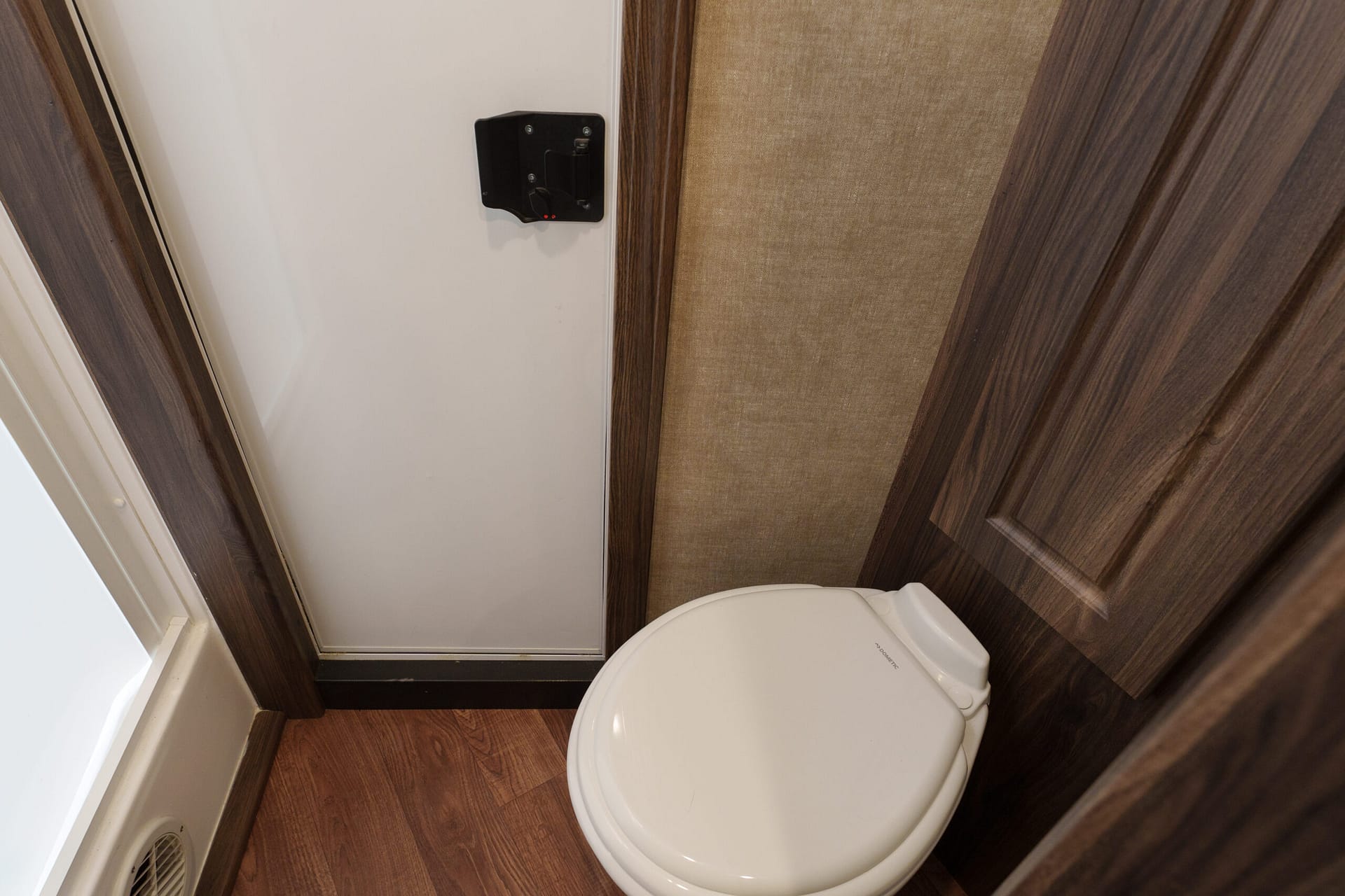 Narrow bathroom with a white toilet beside wood-paneled walls and a floor vent visible near the door.