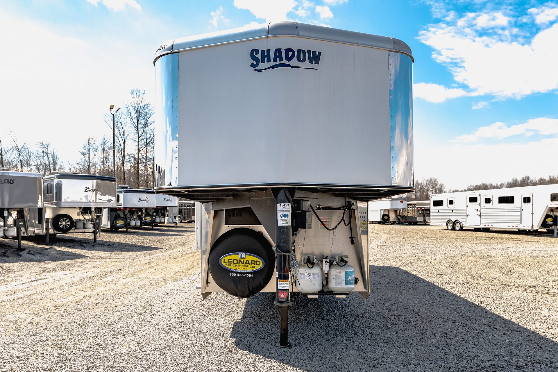 Silver trailer with 'SHADOW' logo in a truck-trailer lot on a sunny day, with other trailers in the background.