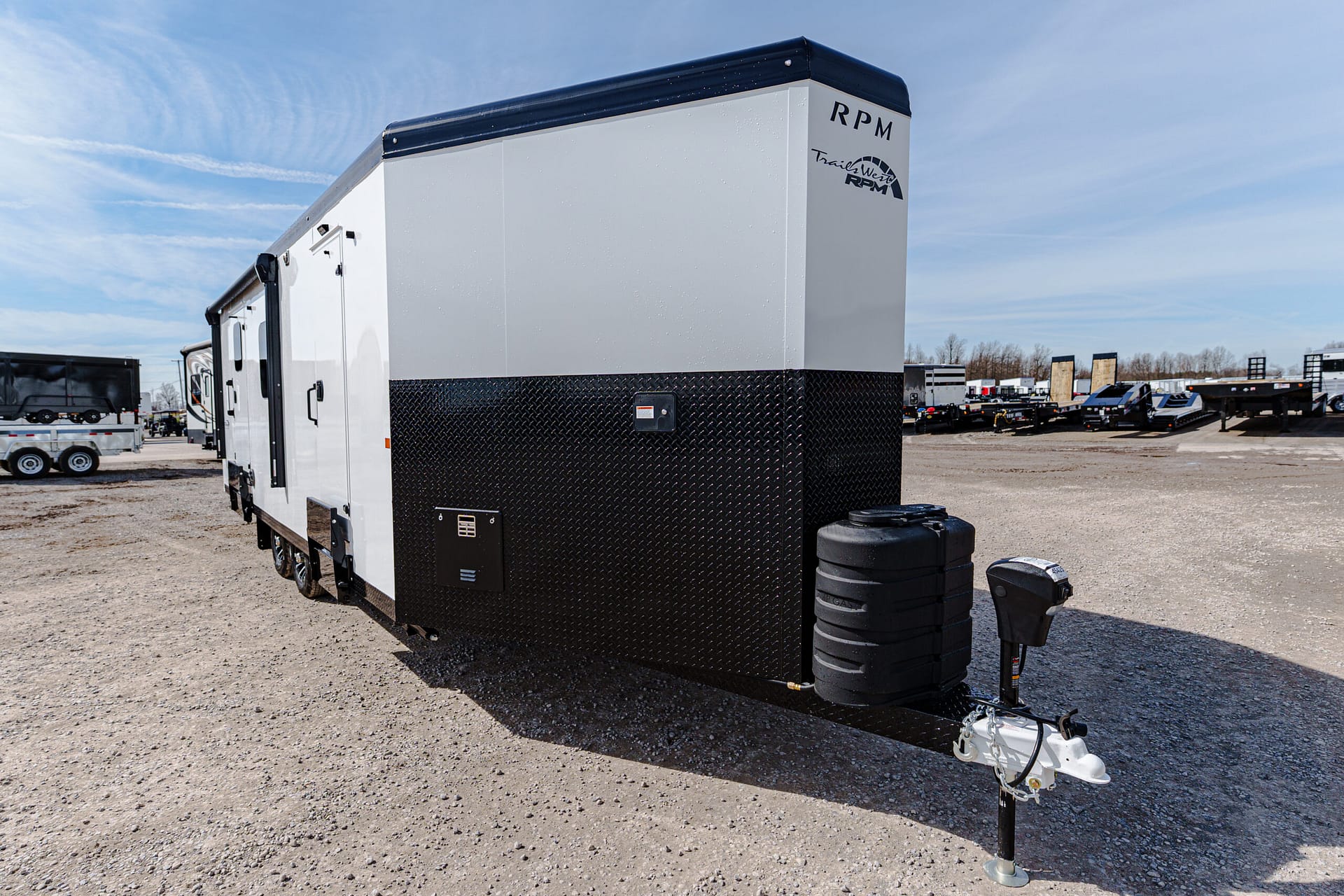 White and black cargo trailer in a lot, front corner visible with diamond-plate lower panel and RPM graphic on the upper right side.