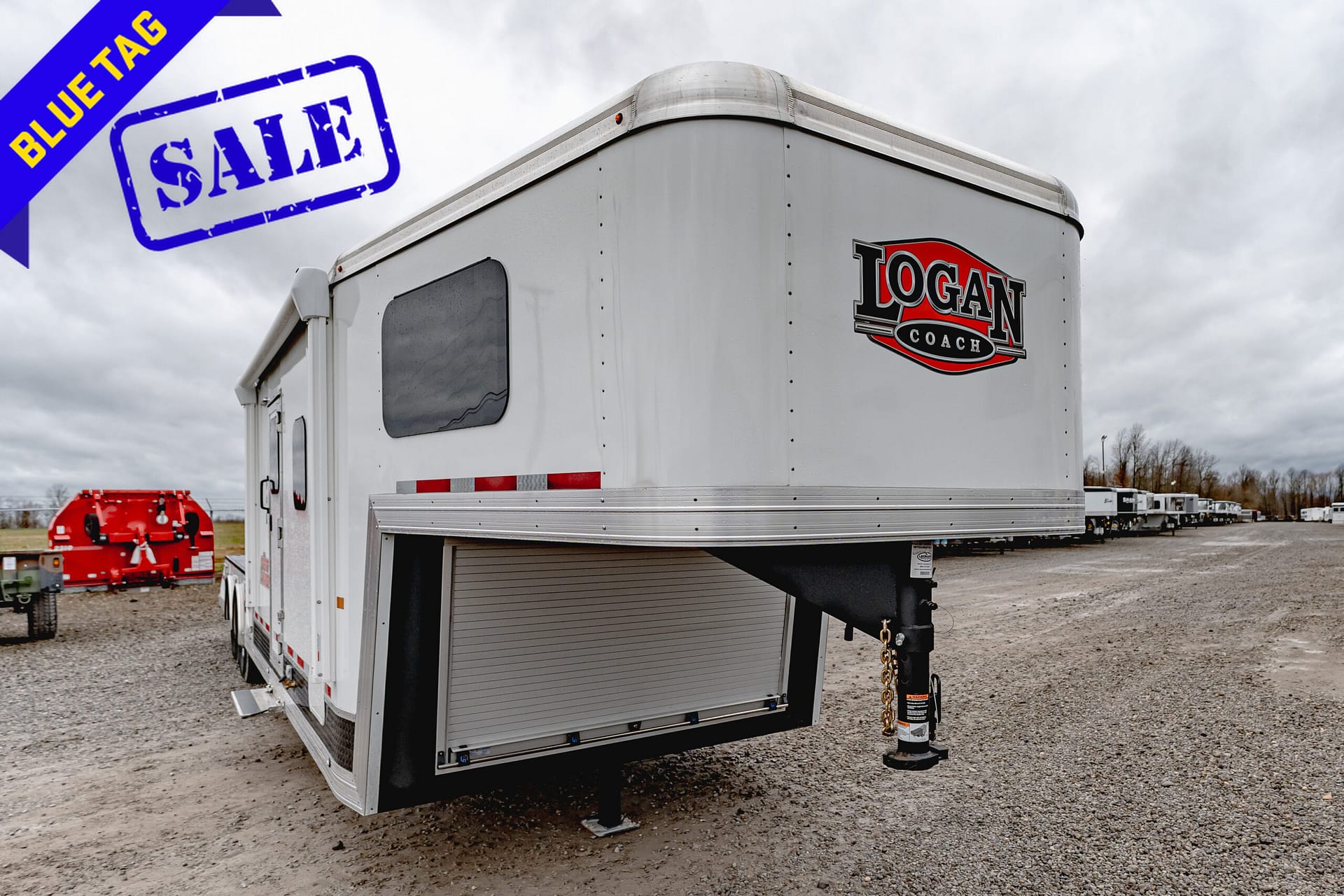 White Logan Coach horse trailer with a large blue SALE stamp and a diagonal blue 'BLUE TAG' ribbon in the foreground.