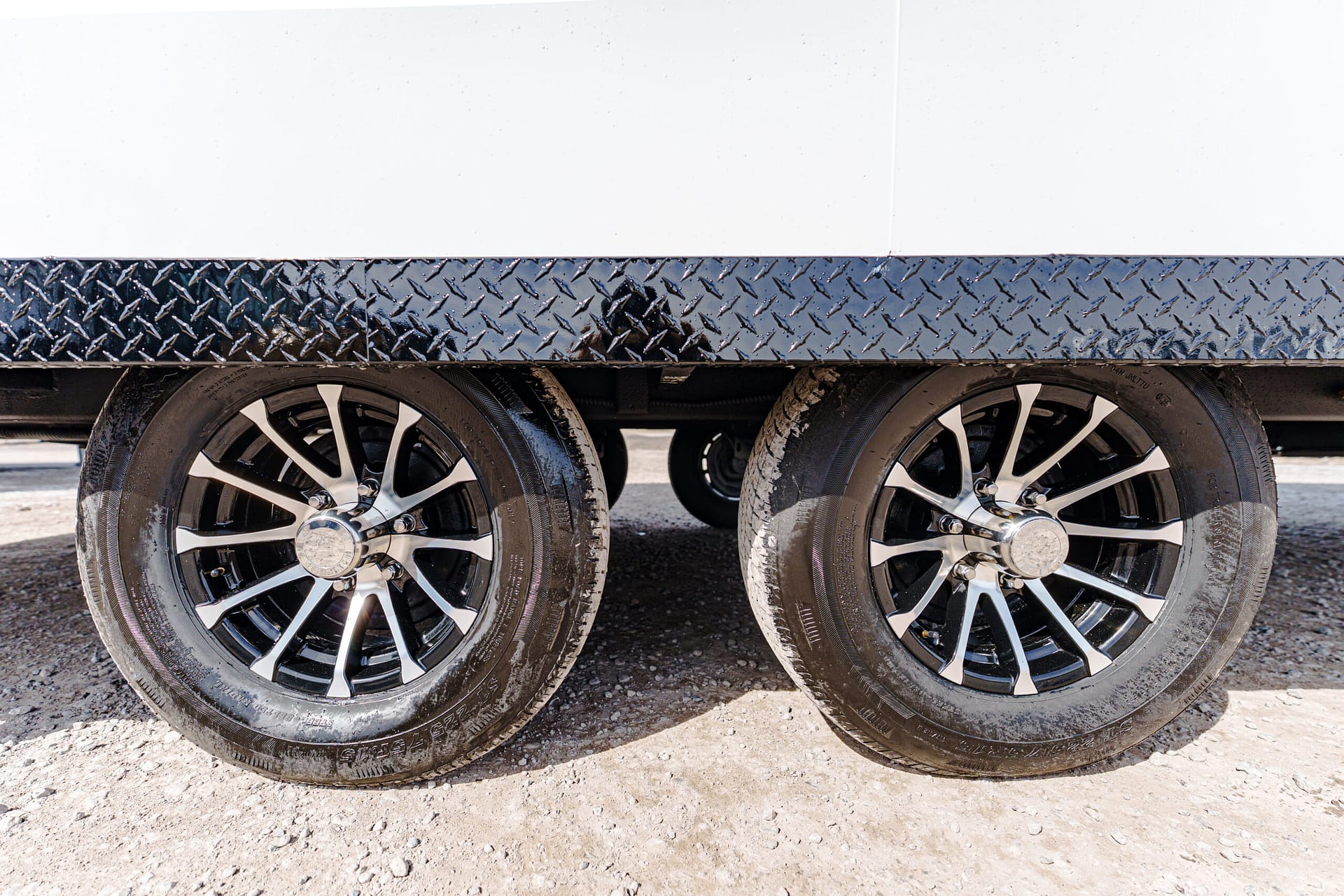 Close-up of two trailer wheels under a diamond-plate side panel on a white trailer.