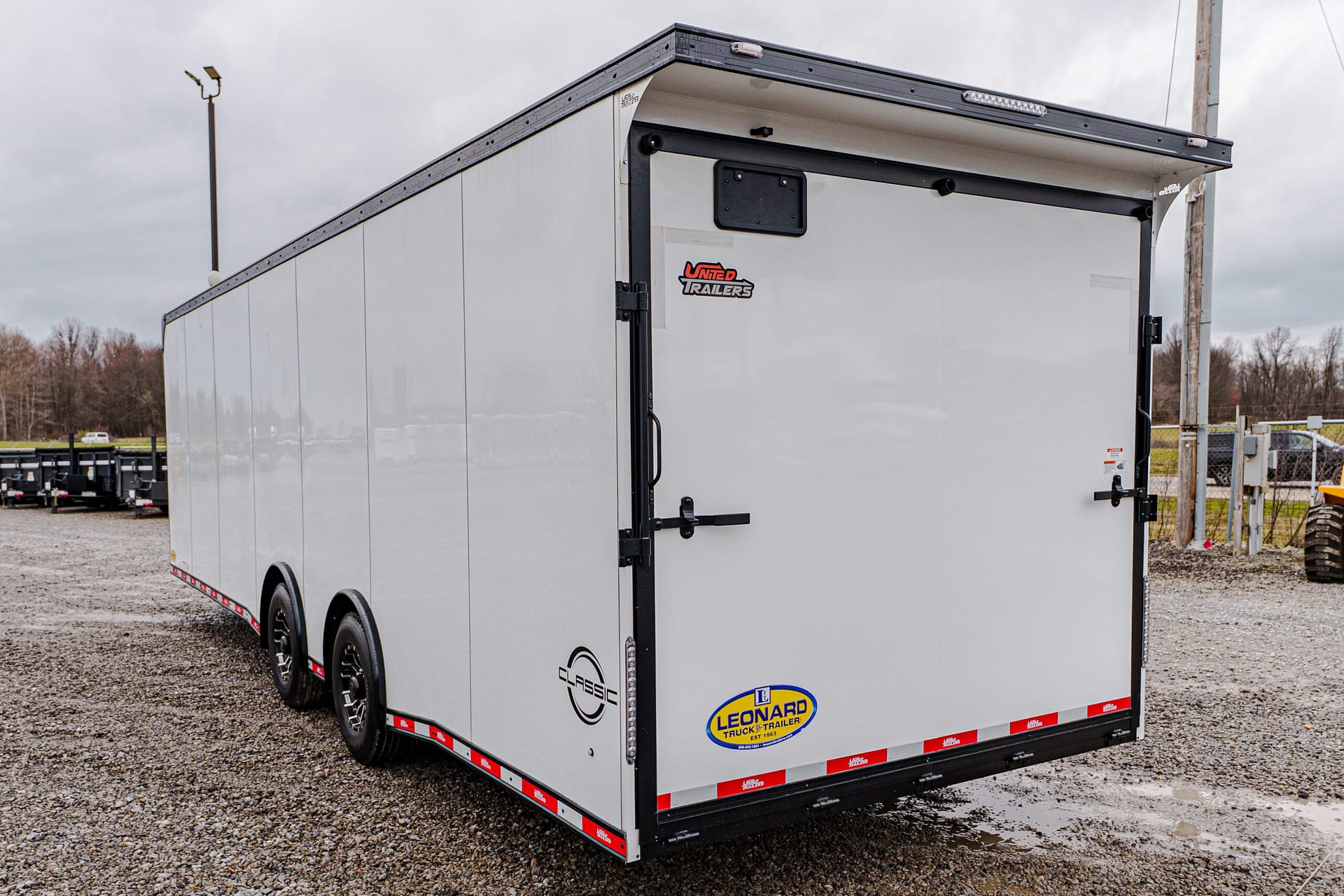 Rear view of a silver enclosed trailer with a Leonard Truck & Trailer logo at a gravel lot.