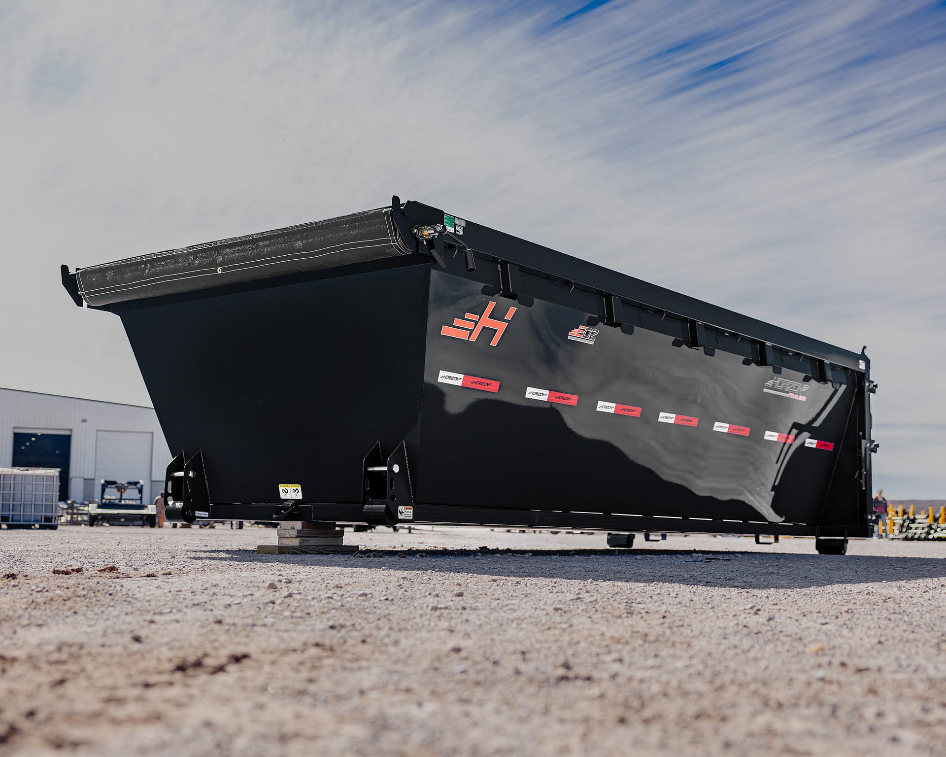 Large black dump trailer bed raised at an industrial site, with red logos and safety stickers along the side.