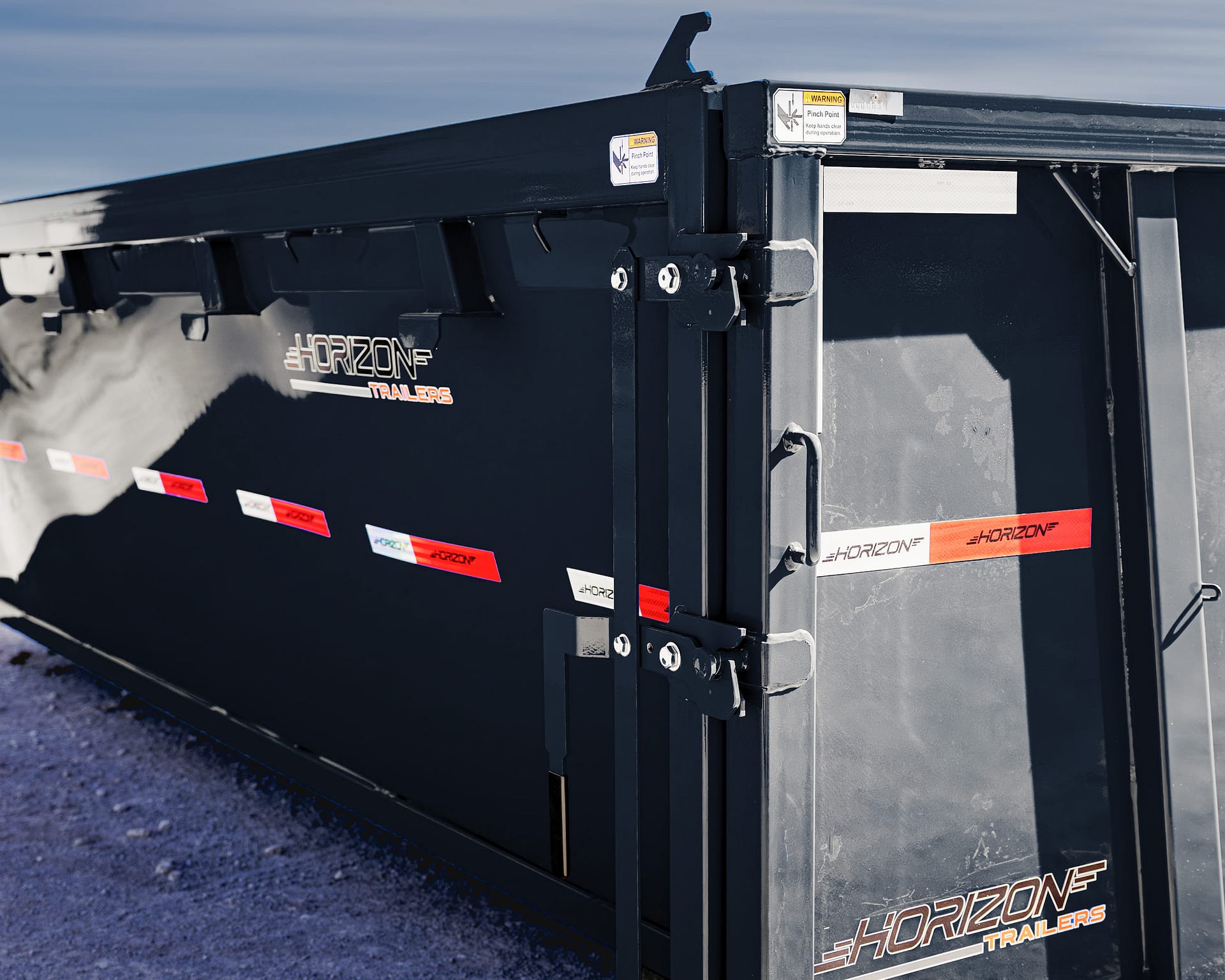 Rear corner of a black Horizon Trailers utility trailer with safety stickers and metal latches visible.
