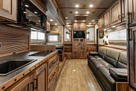 Living_Quarters_Bloomer_Interior4 – Leonard Truck and Trailer, Inc Interior of a wood-toned RV kitchen and living area with a leather sofa and a mounted TV on the back wall
