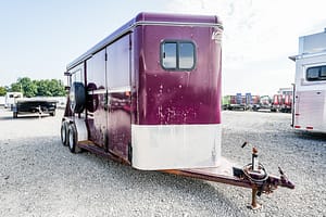 Image 0 for SKU 46558 – Leonard Truck and Trailer, Inc Maroon gooseneck horse trailer with a diamond-plate front parked on a gravel lot; spare tire mounted on the side and a hitch in the foreground with other trailers in the background